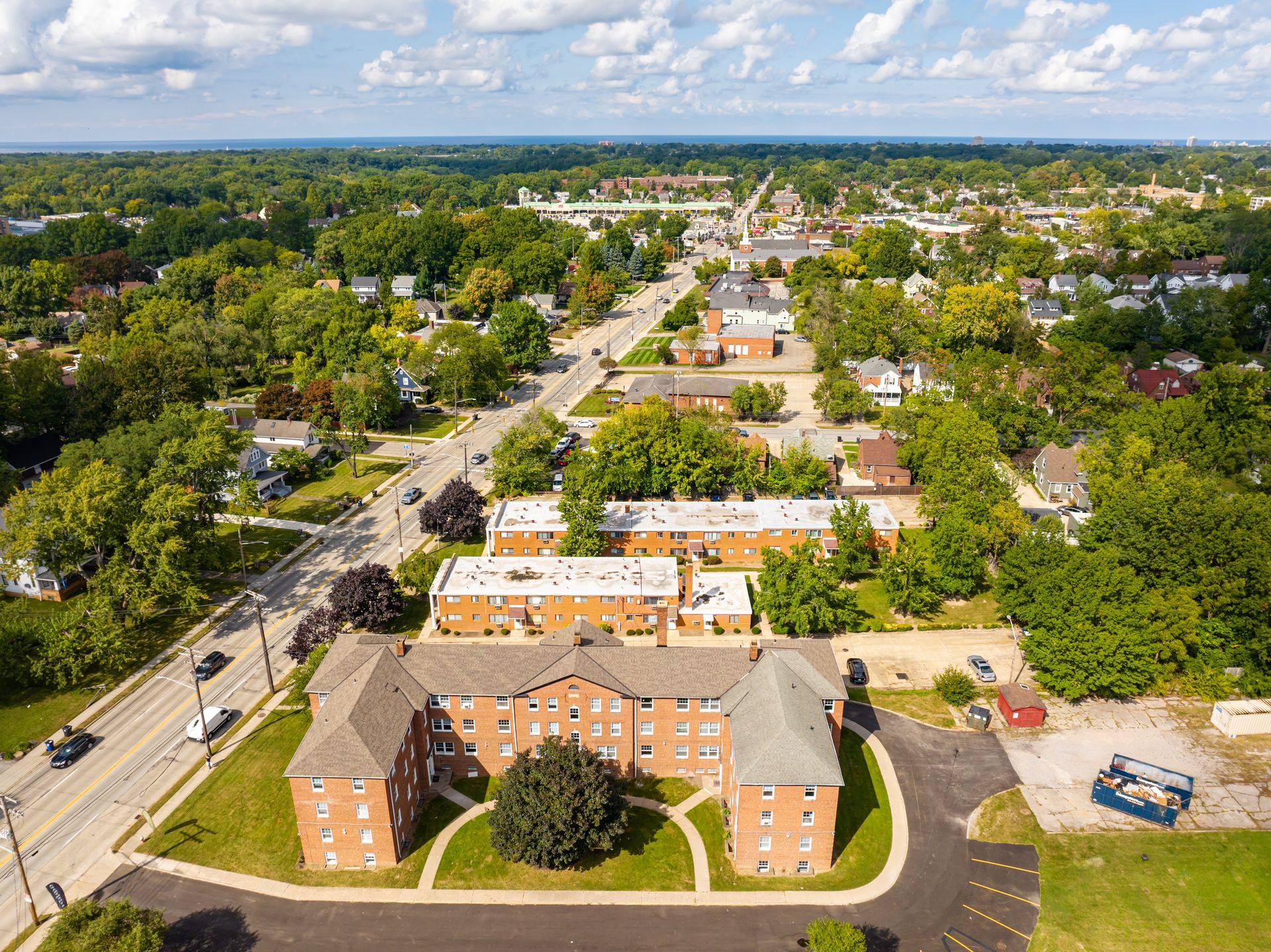 Aerial view of a brick apartment building and a street in a town surrounded by green trees.