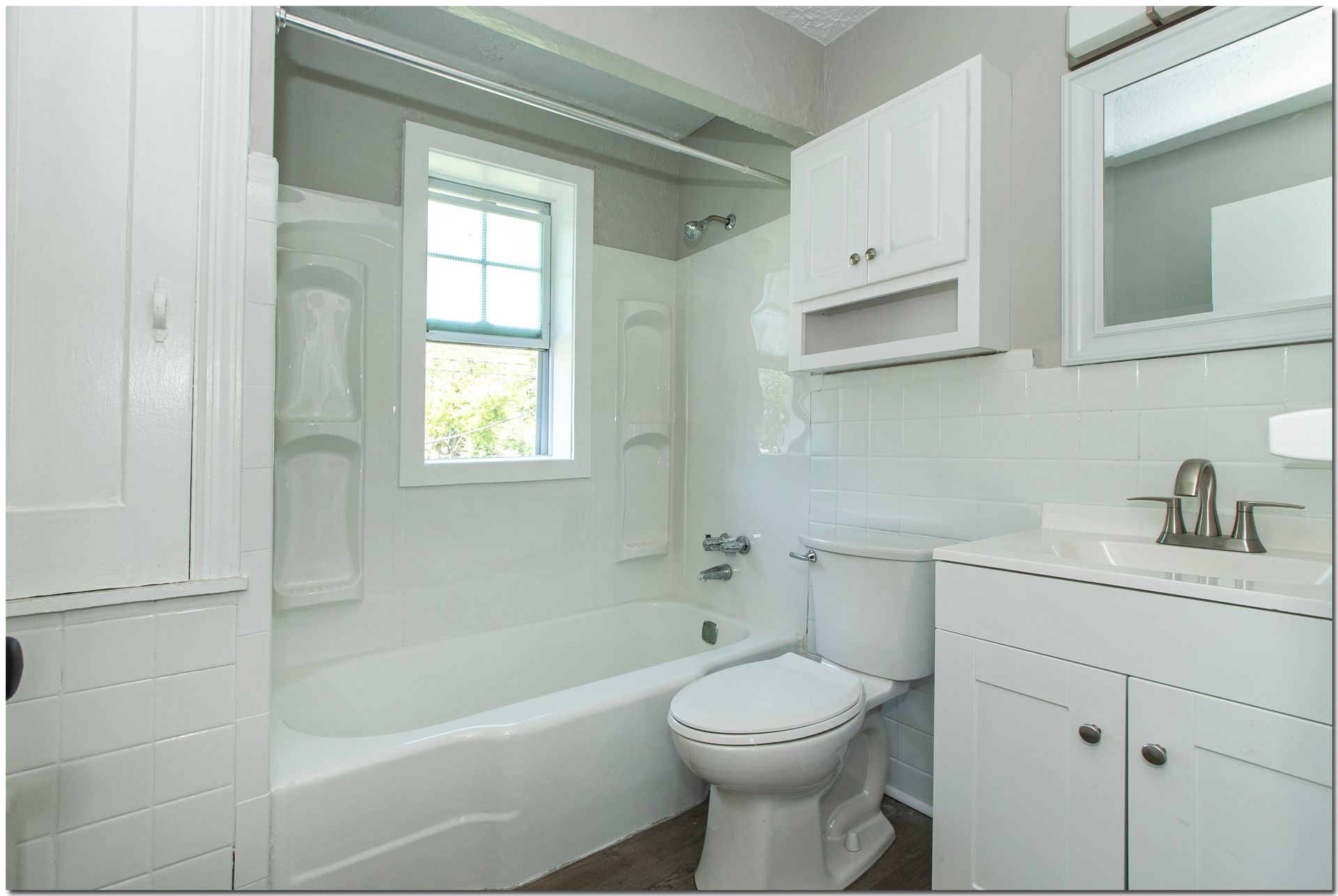 White bathroom with a tub, toilet, vanity, and window.