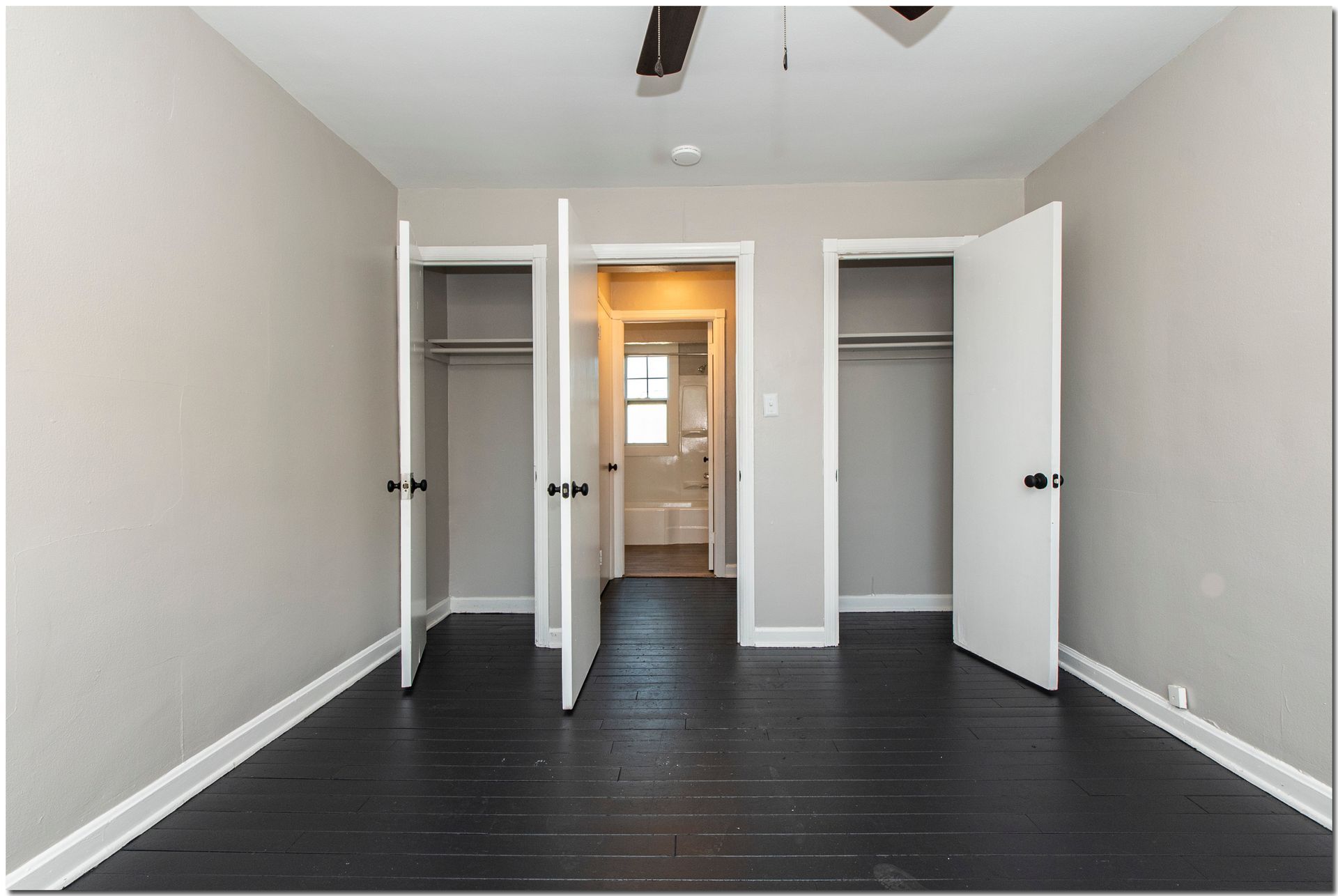 Bedroom with dark wood floor, white walls, three closets with open doors, and a view into a bathroom.