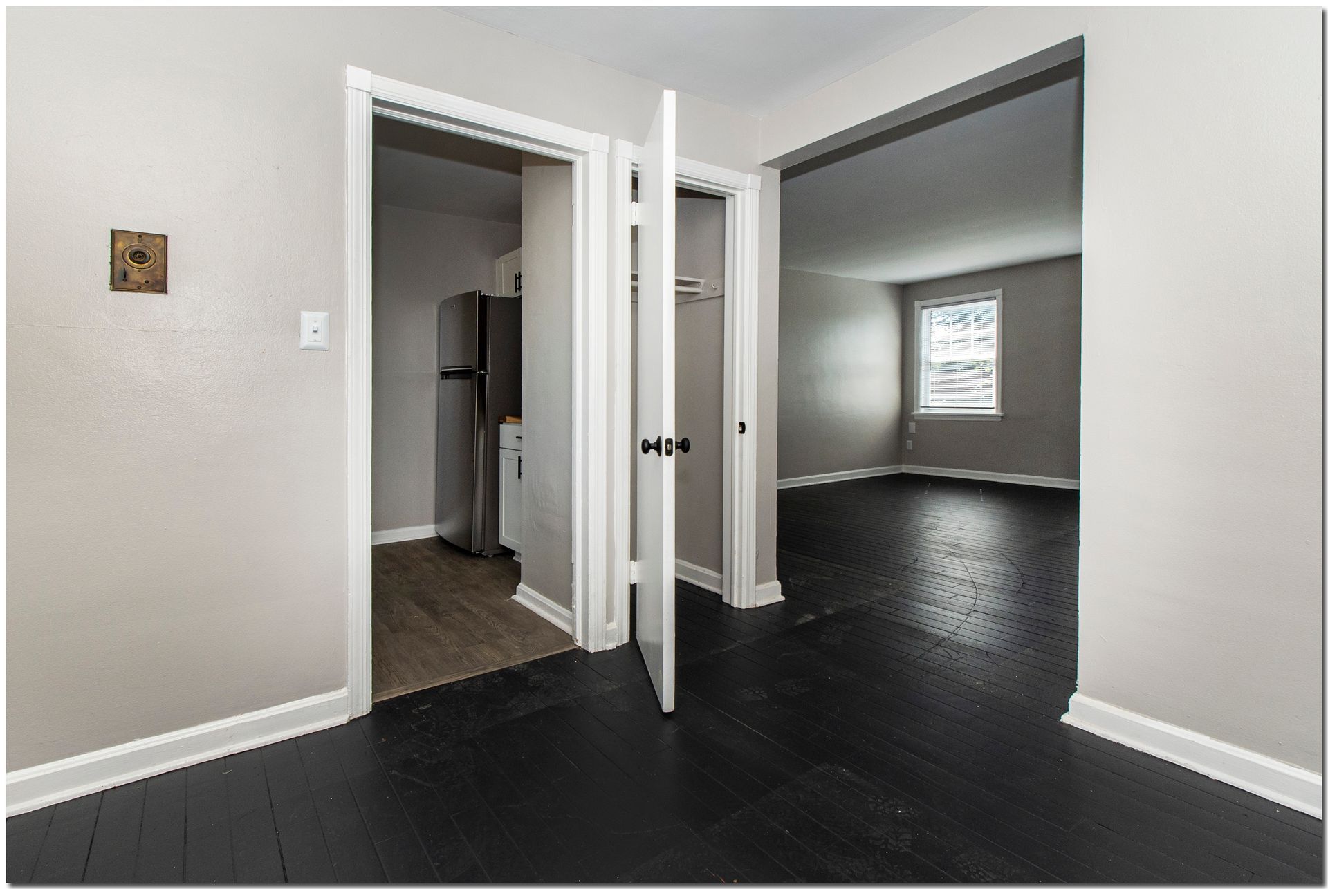 Interior view of an apartment with dark wood floors, open doorways to a kitchen and a living area.