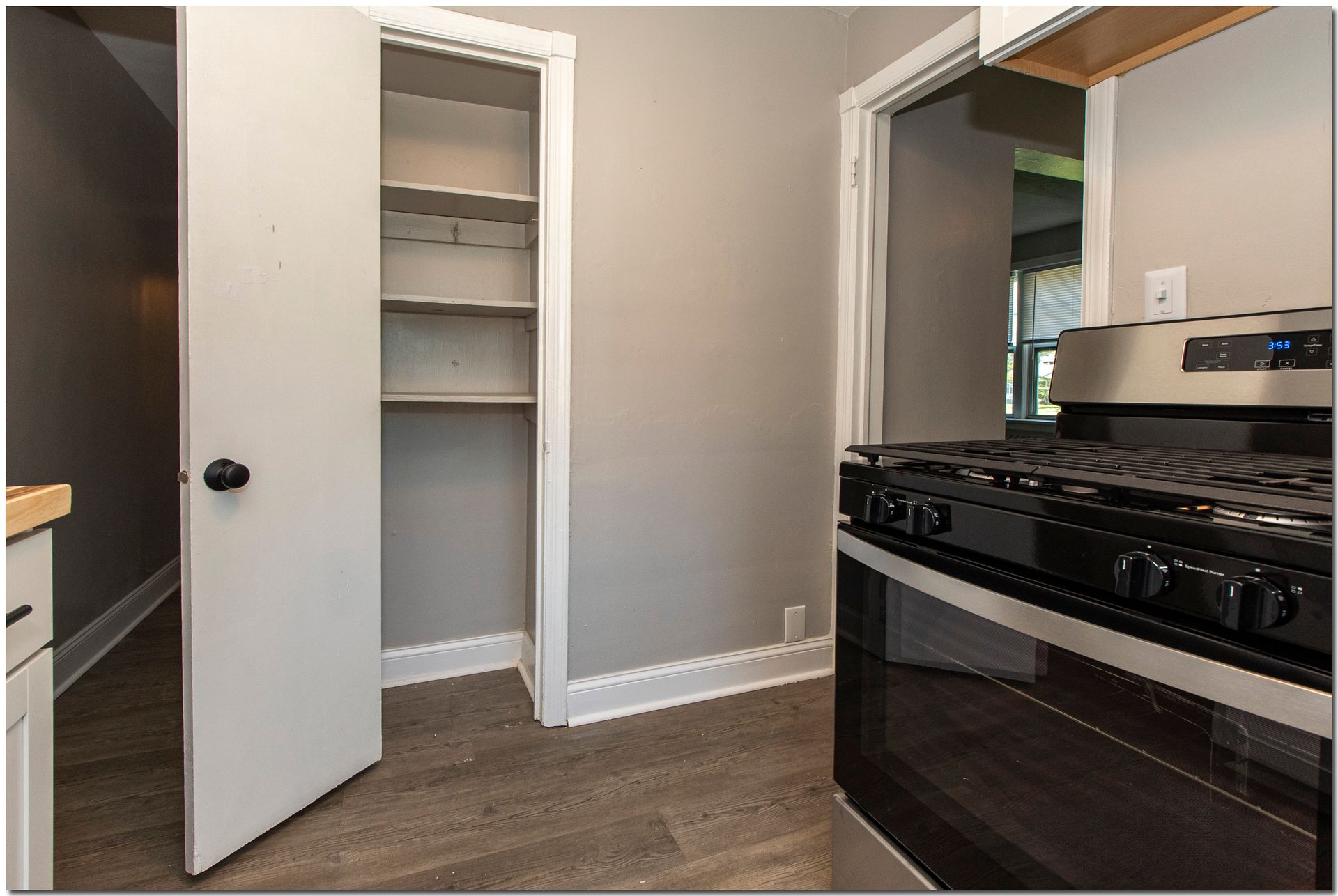 Kitchen with pantry, gray walls, gas stove, and wood-look flooring.