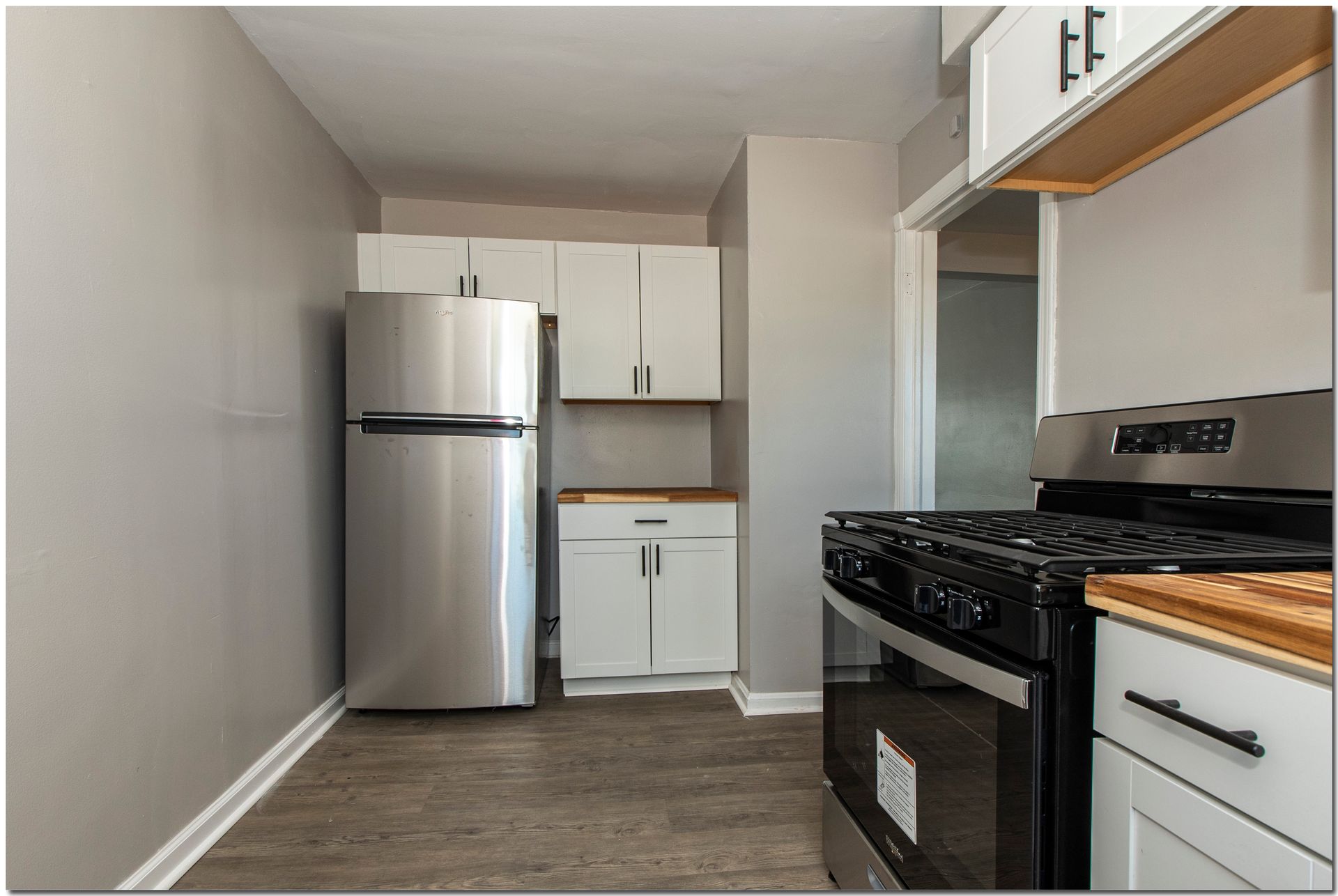 Small kitchen with stainless steel appliances and white cabinets against gray walls.