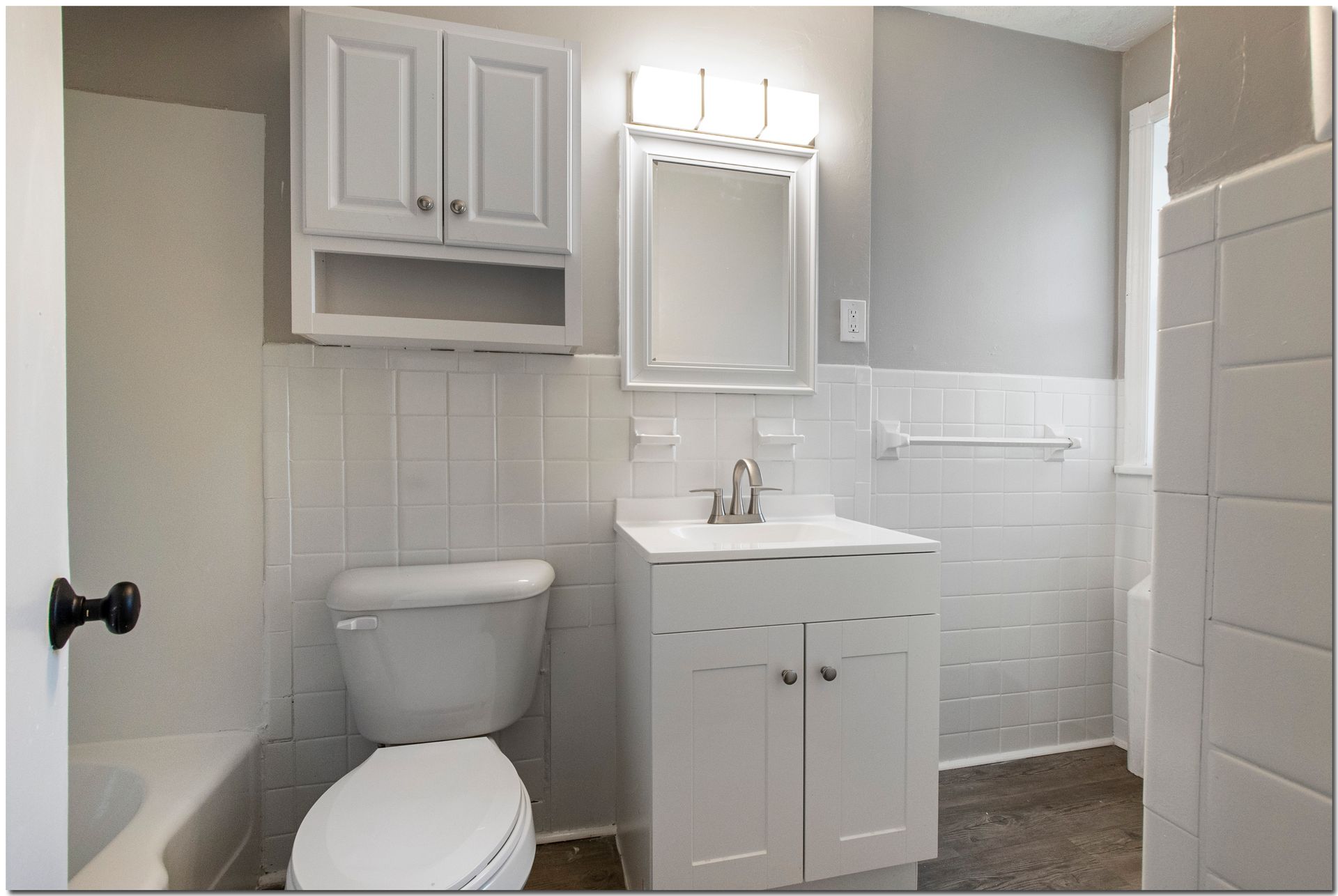 White bathroom with toilet, sink, and medicine cabinet; light gray walls and dark floor.