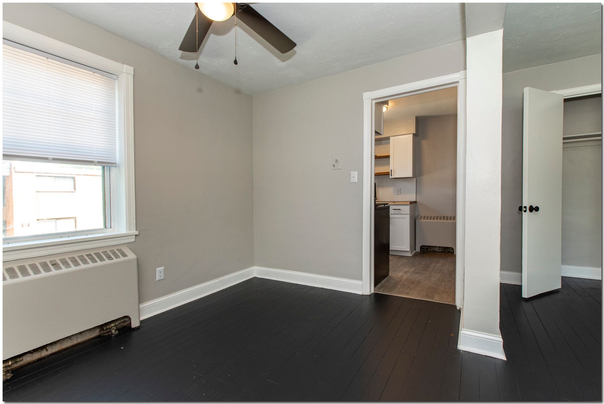 Bedroom with dark wood floor, pale gray walls, and open doorway to kitchen.