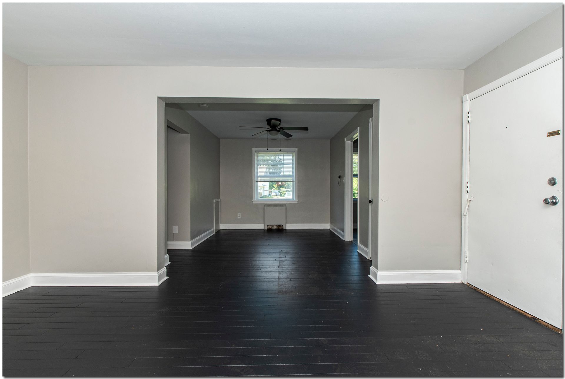 Room interior with dark wood floor, light gray walls, and an open doorway to another room.