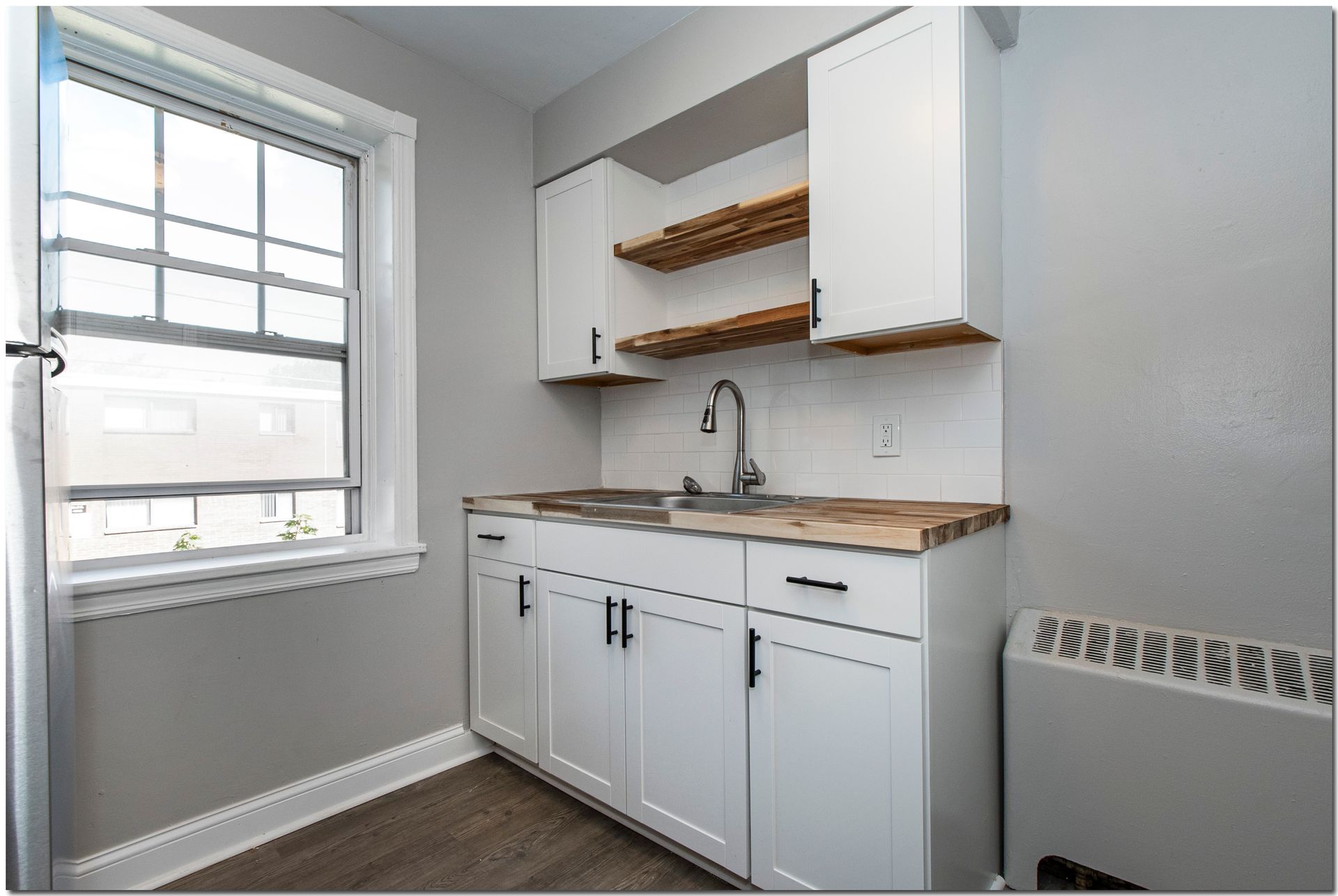Small kitchenette with white cabinets, sink, and window. Includes wooden shelves and countertop.