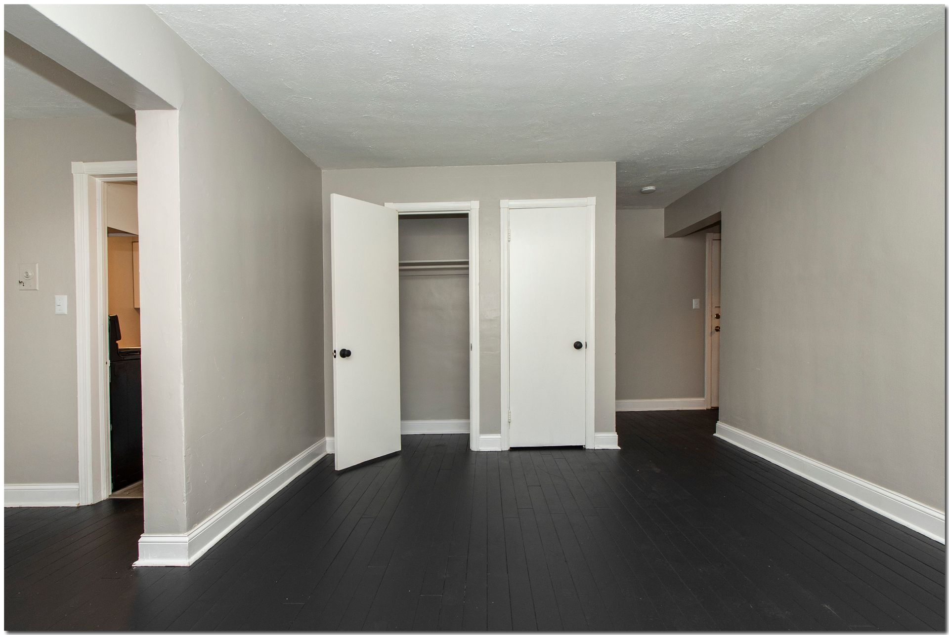 Empty room with dark floor, light grey walls, white doors and trim.