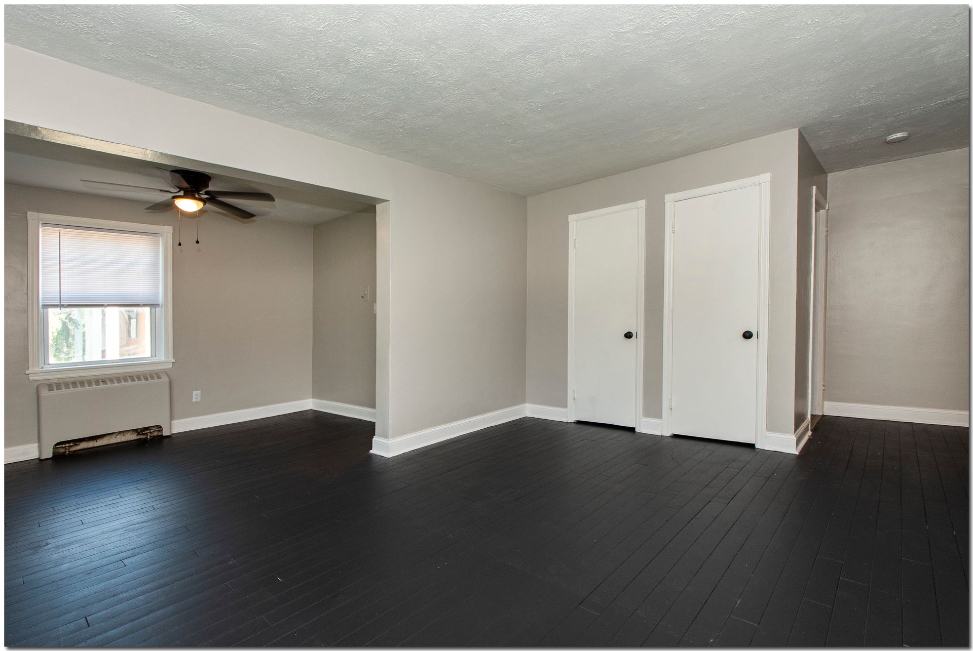 Empty room with gray walls, black floor, white doors, and a window with blinds.