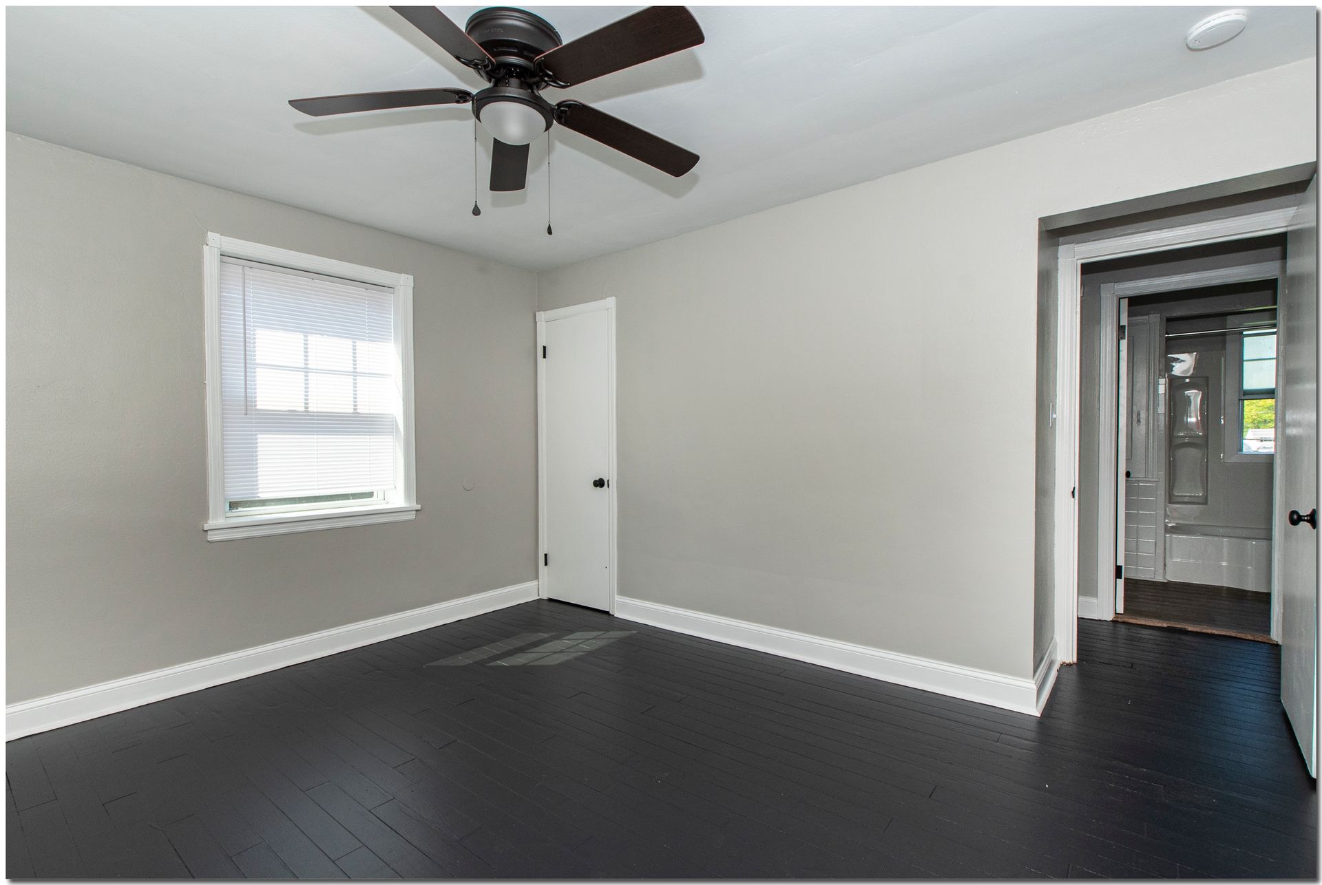 Bedroom with gray walls, dark wood floors, and a ceiling fan. Doorway visible.