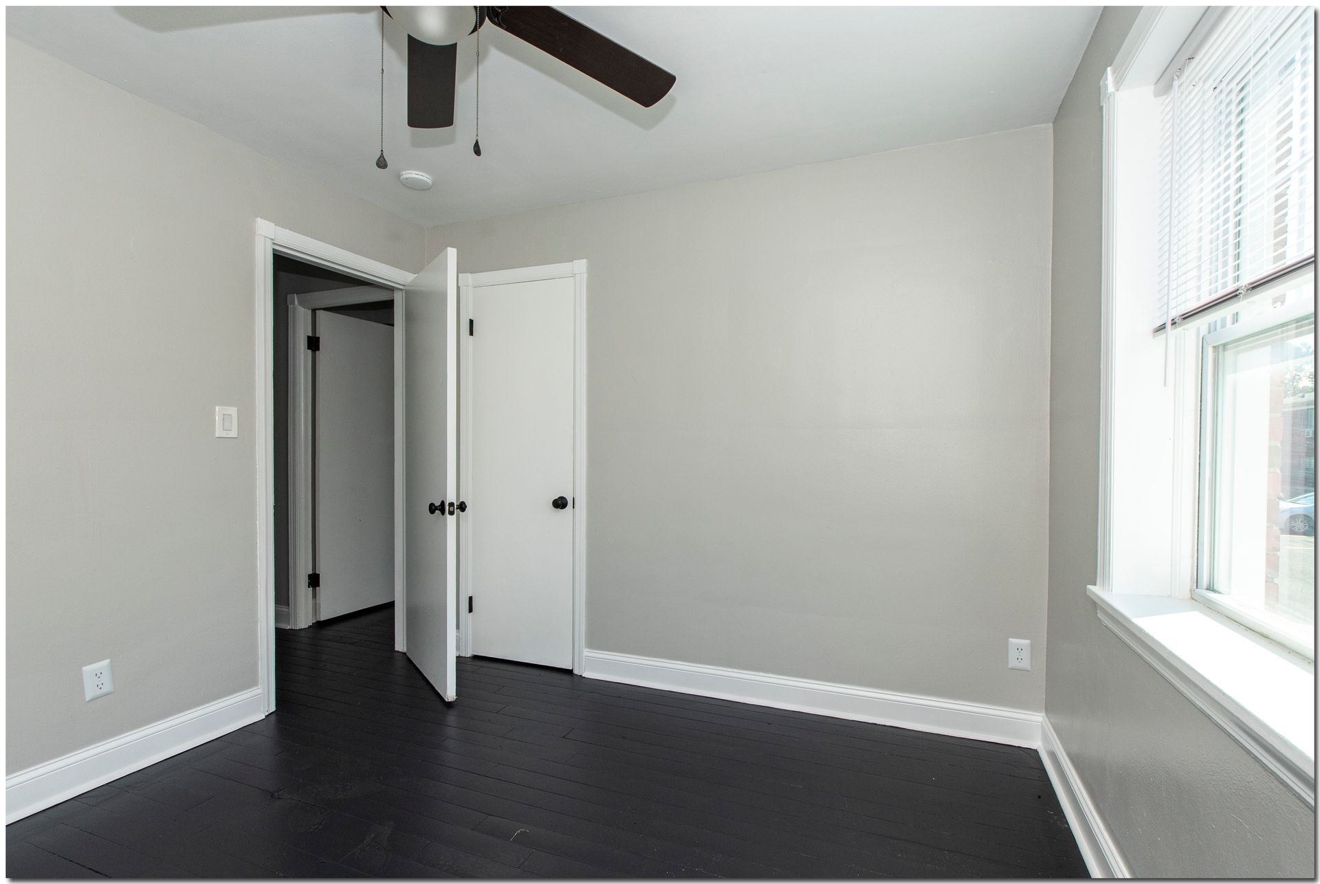 Bedroom with gray walls, dark wood floor, white trim, and a window with blinds.