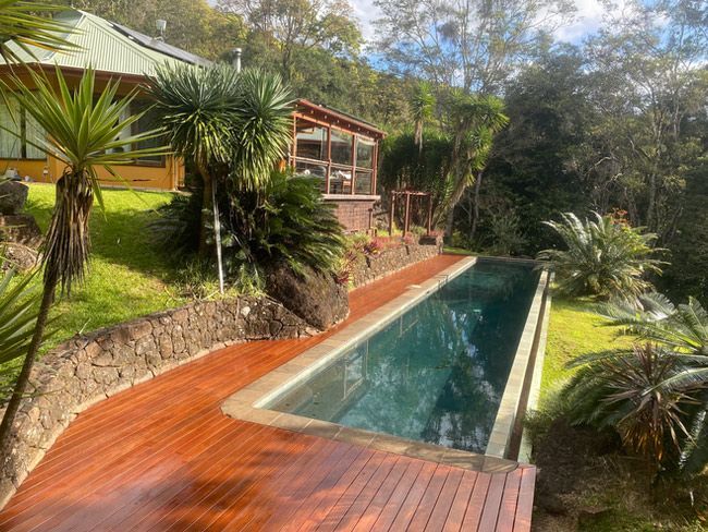 A Large Swimming Pool Is Surrounded By Trees And A Wooden Deck — Green e Building in Lennox Head, NSW