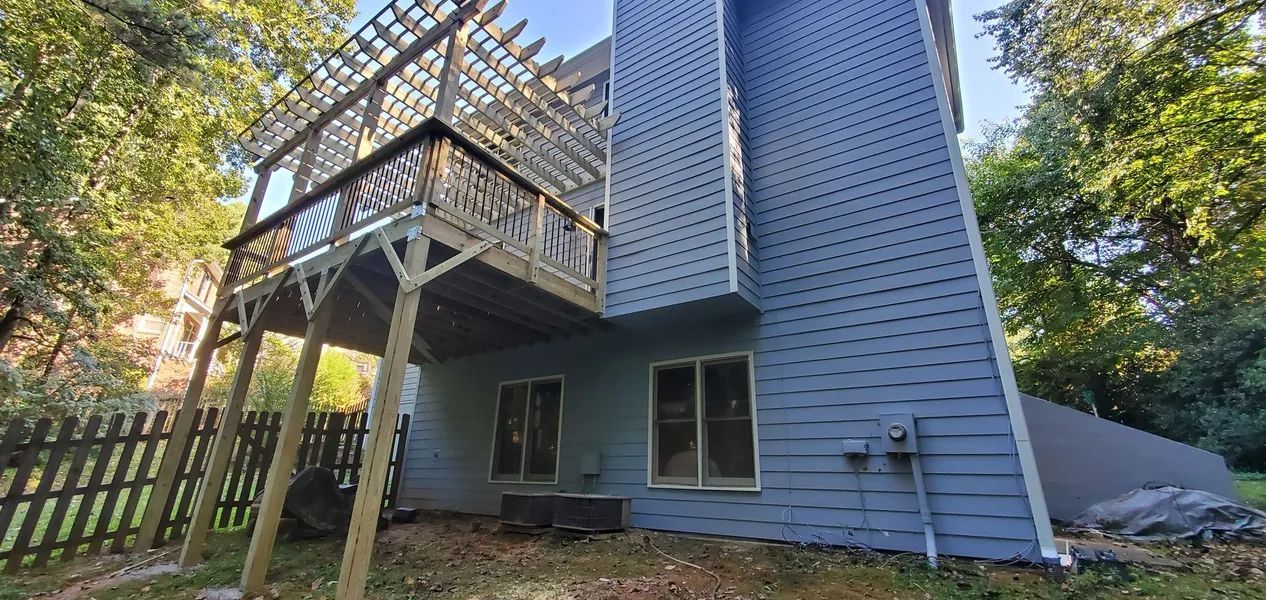 Back of a two-story house with a deck, surrounded by trees. Blue siding, brown wooden deck.