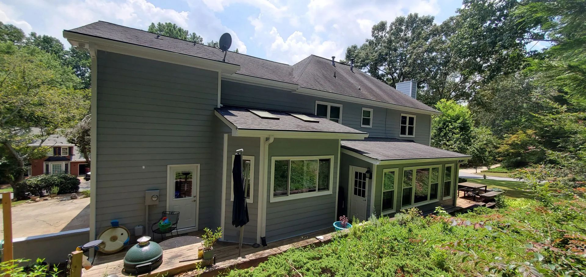 Exterior view of a gray two-story house with a porch and surrounding greenery on a sunny day.