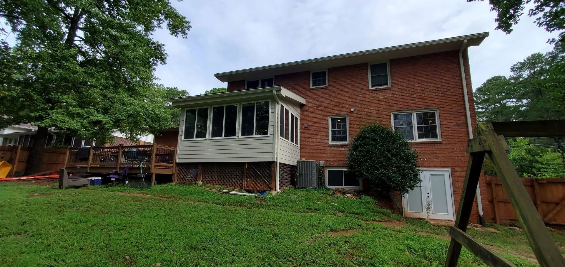 Brick house with a sunroom, deck, and grassy backyard.