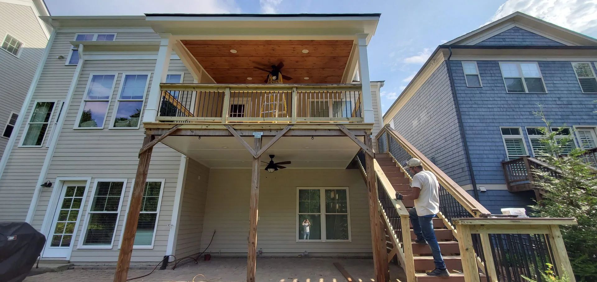 Back of a light-colored house with a raised deck and stairs. Man climbing the stairs.