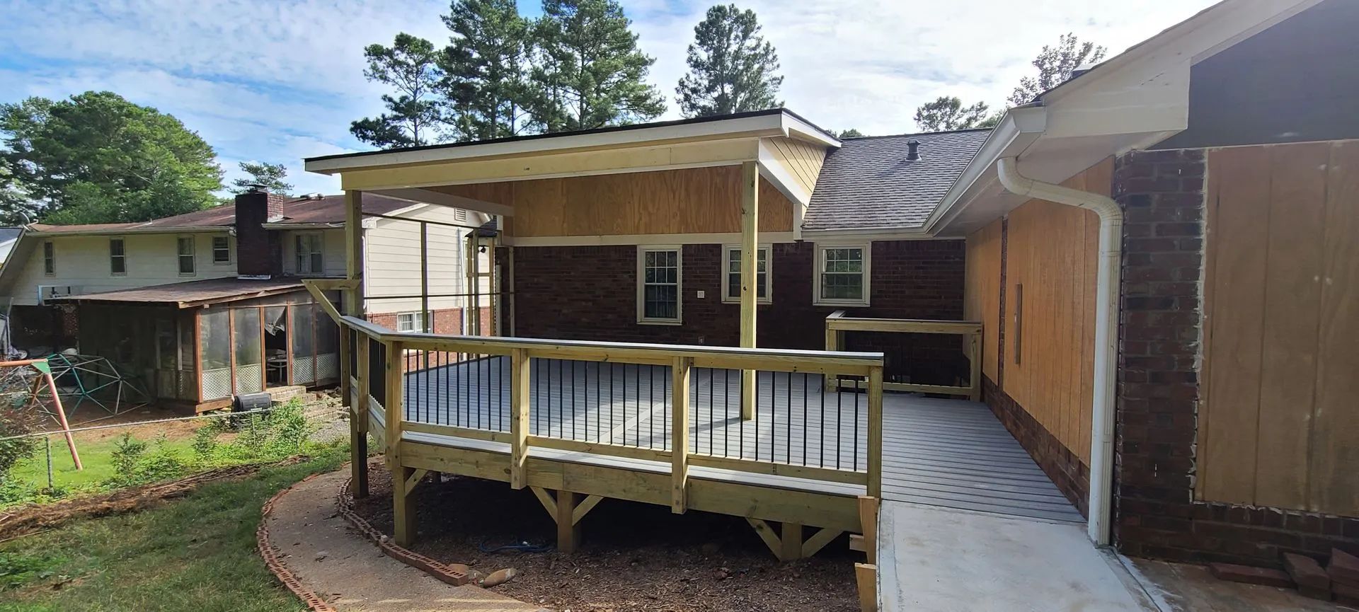 A new wooden deck with a covered area next to a brick house.