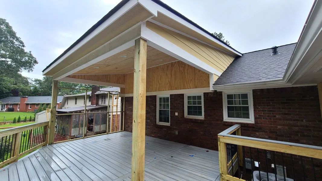 Backyard deck with new wooden awning over a brick house; gray decking, white trim, and wooden supports.