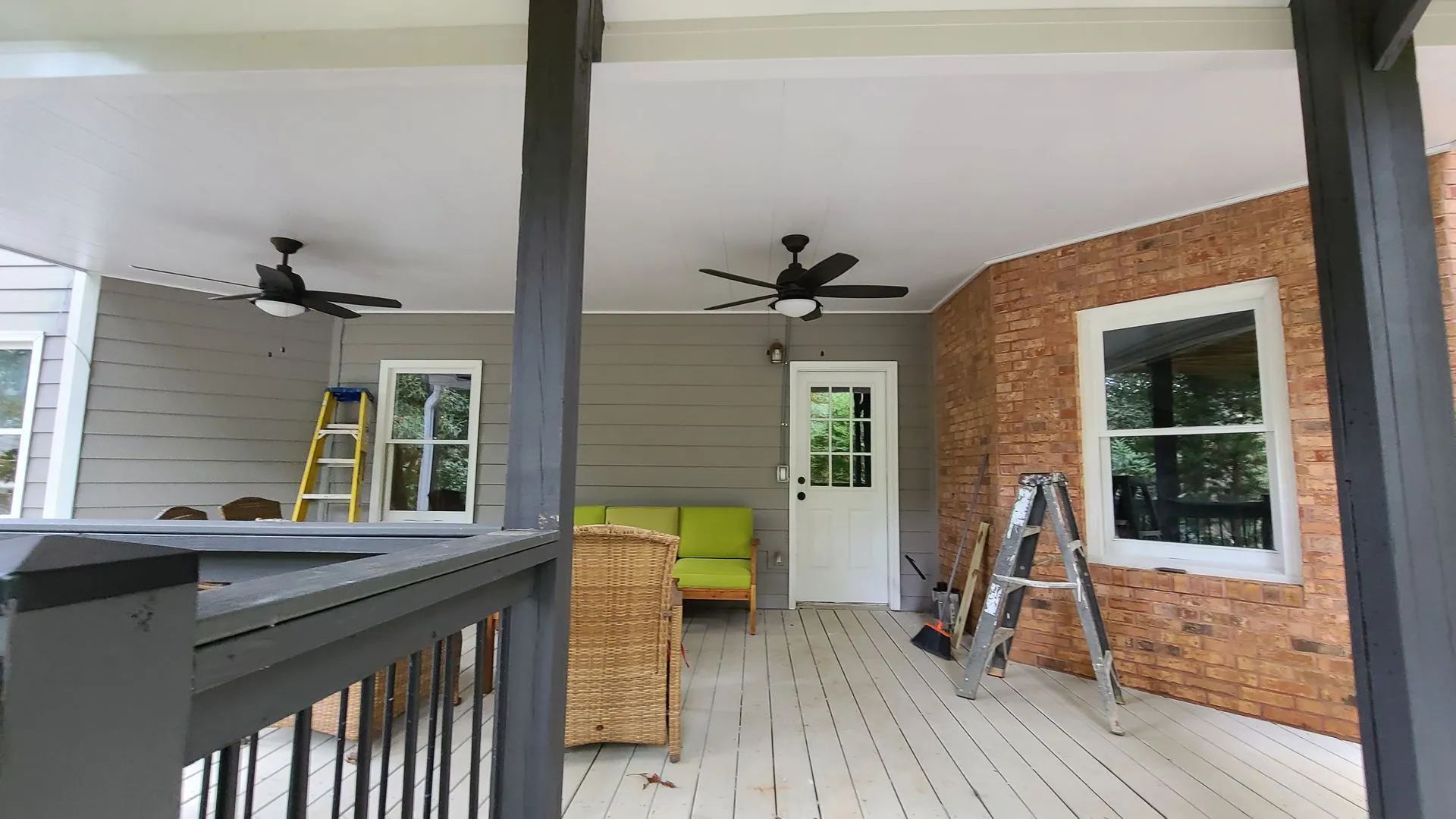 Covered porch with ceiling fans, a brick wall, and gray and white painted surfaces.