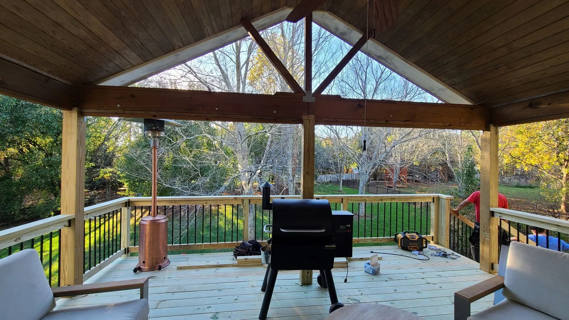 Covered deck with a smoker, heater, and trees in the background.