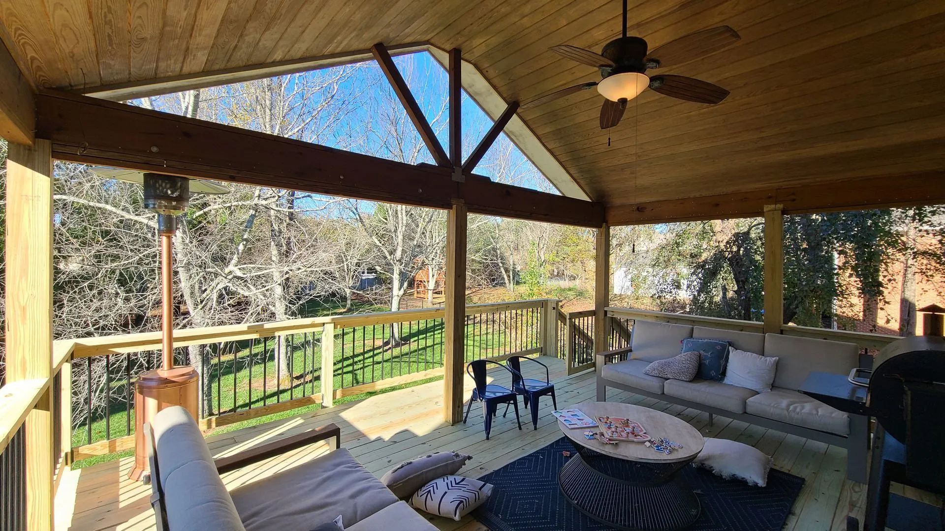 Covered wooden deck with outdoor furniture, a ceiling fan, and a view of trees and grass.