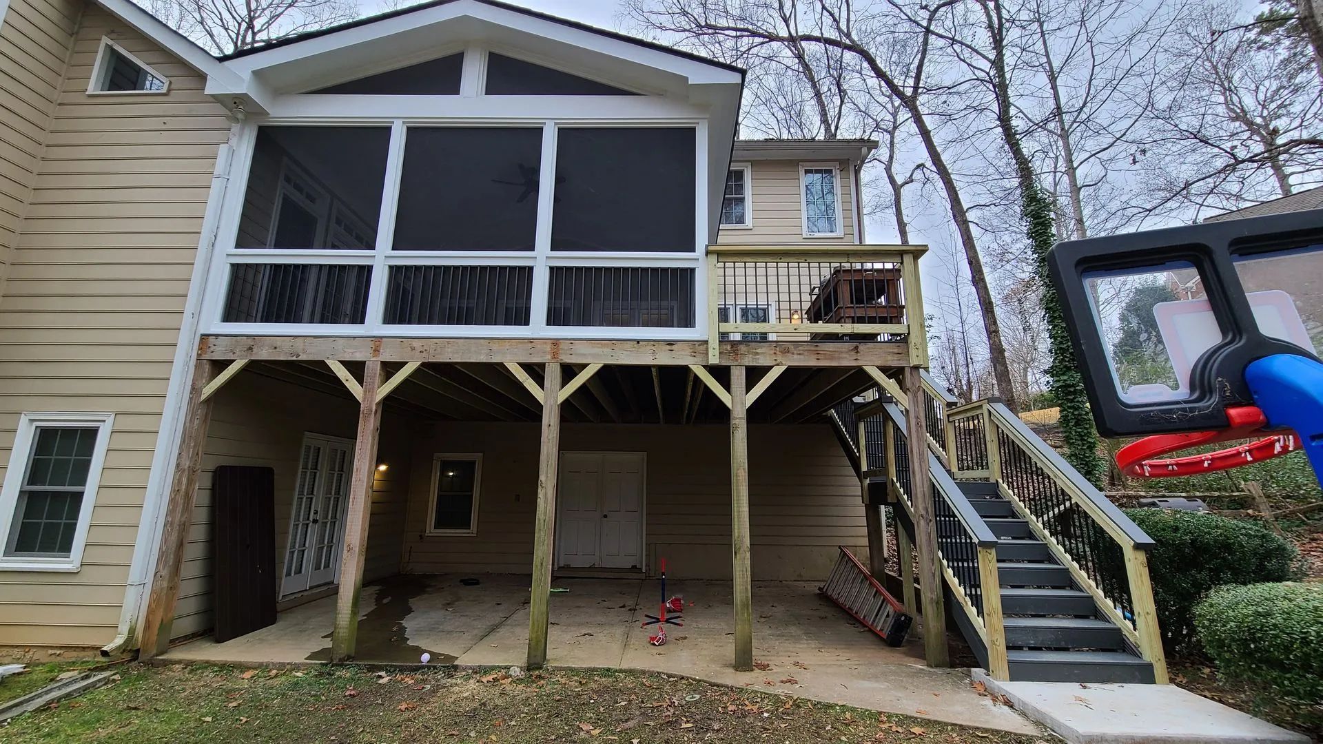 Back of house with screened porch, deck, and stairs. Basketball hoop visible. Cloudy day.