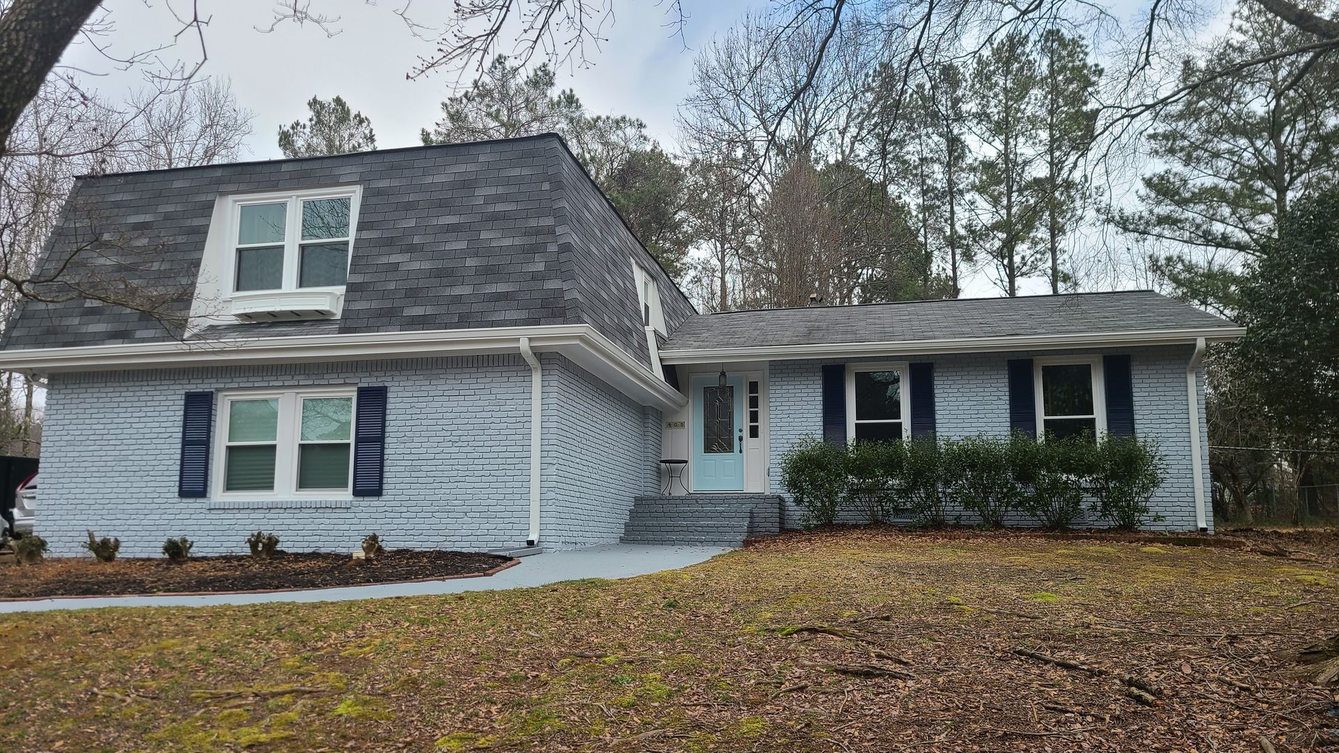 Two-story house with gray brick, blue shutters, and a light blue door. Front yard with dry grass.