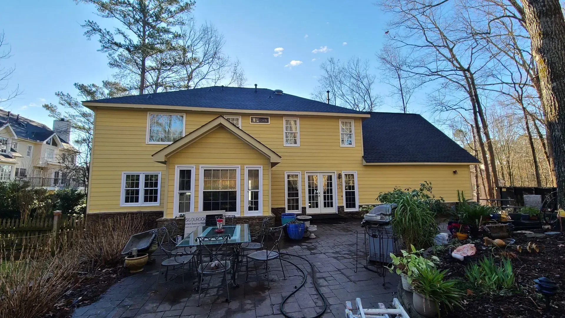 Back of a two-story yellow house with dark roof, multiple windows, and patio furniture on the ground.