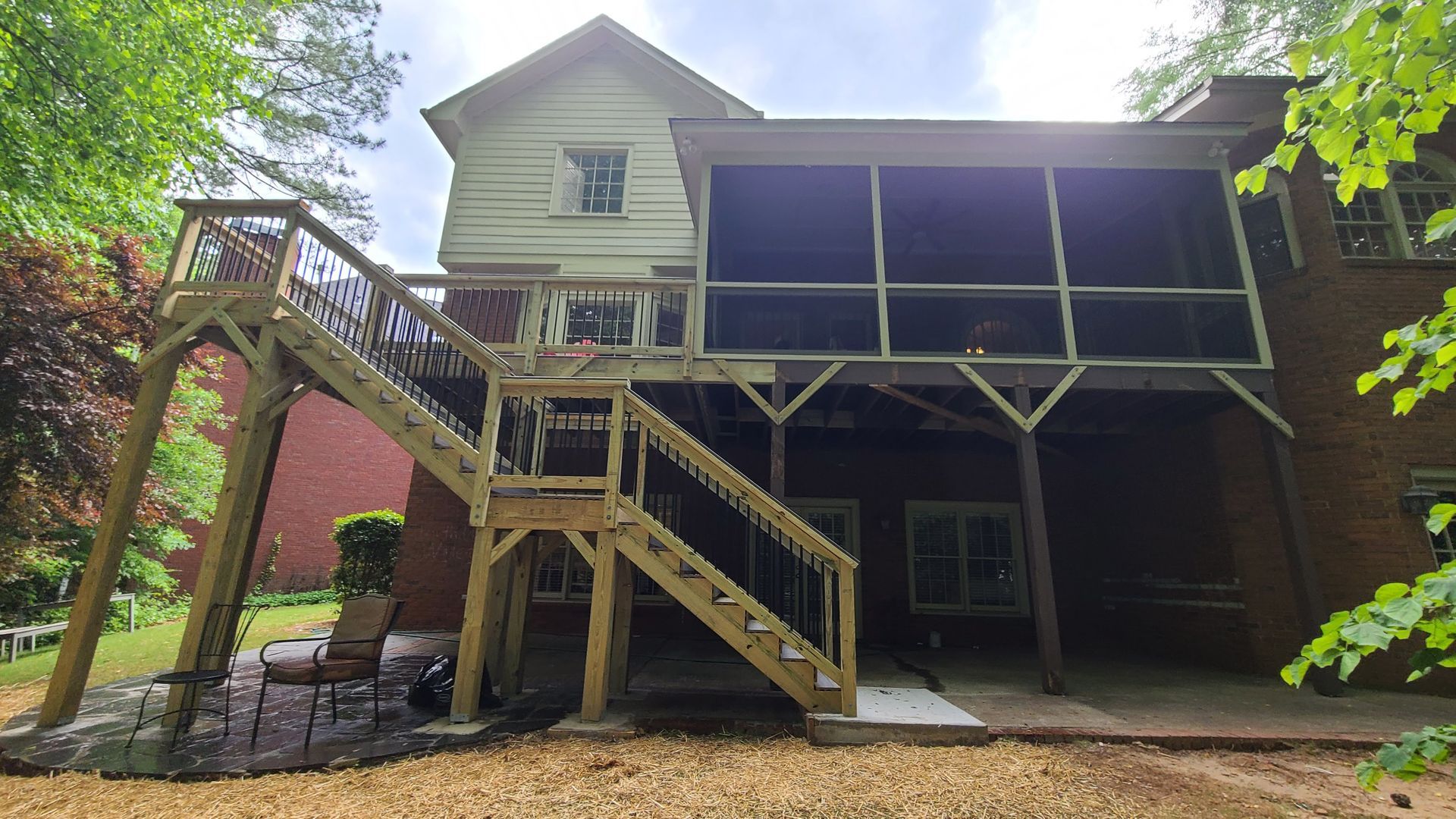 Wooden deck with stairs, screened porch attached to a brick house.