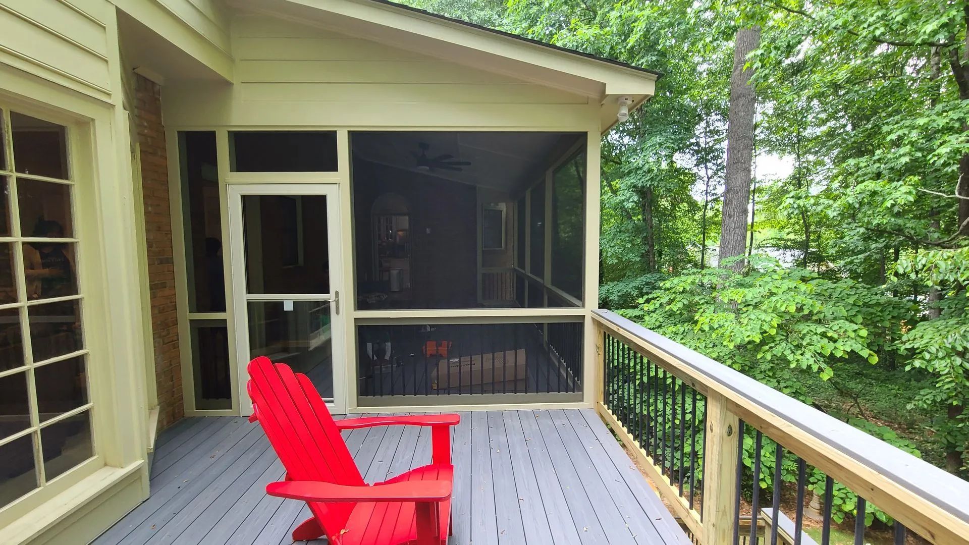 Red chair on screened porch with deck overlooking trees.