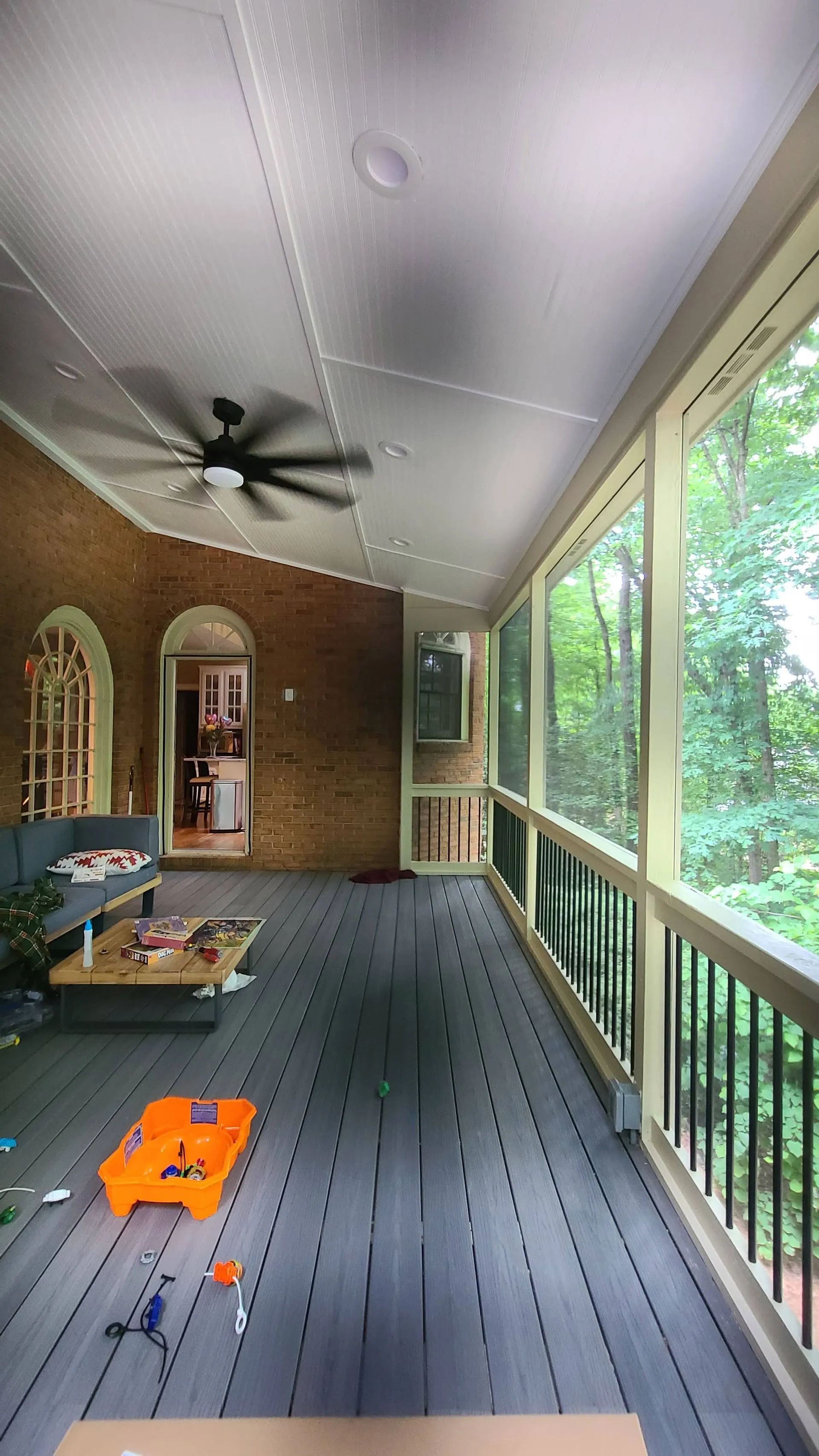 Screened porch with brick wall, gray floor, and lush green trees visible outside windows.
