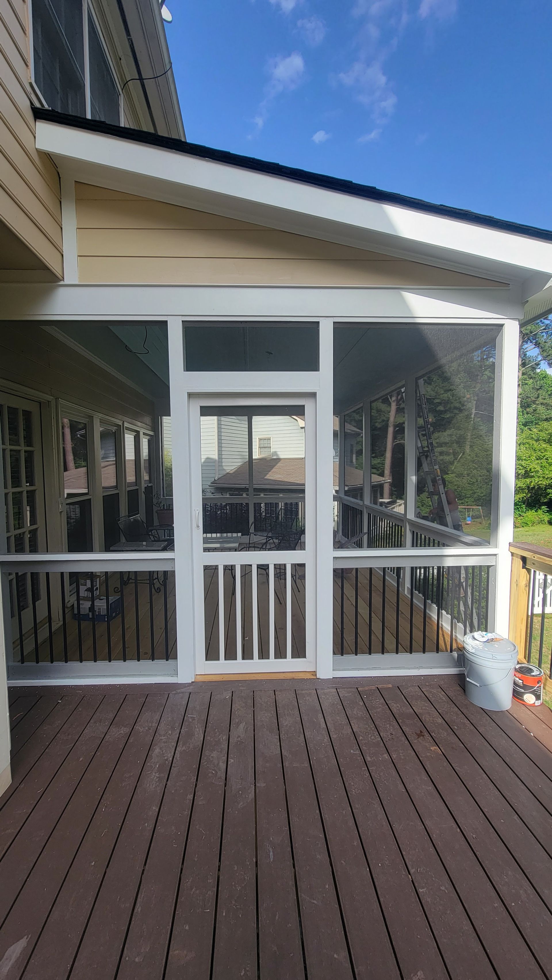 Screened-in porch with white trim, wooden deck, door, and white bucket.
