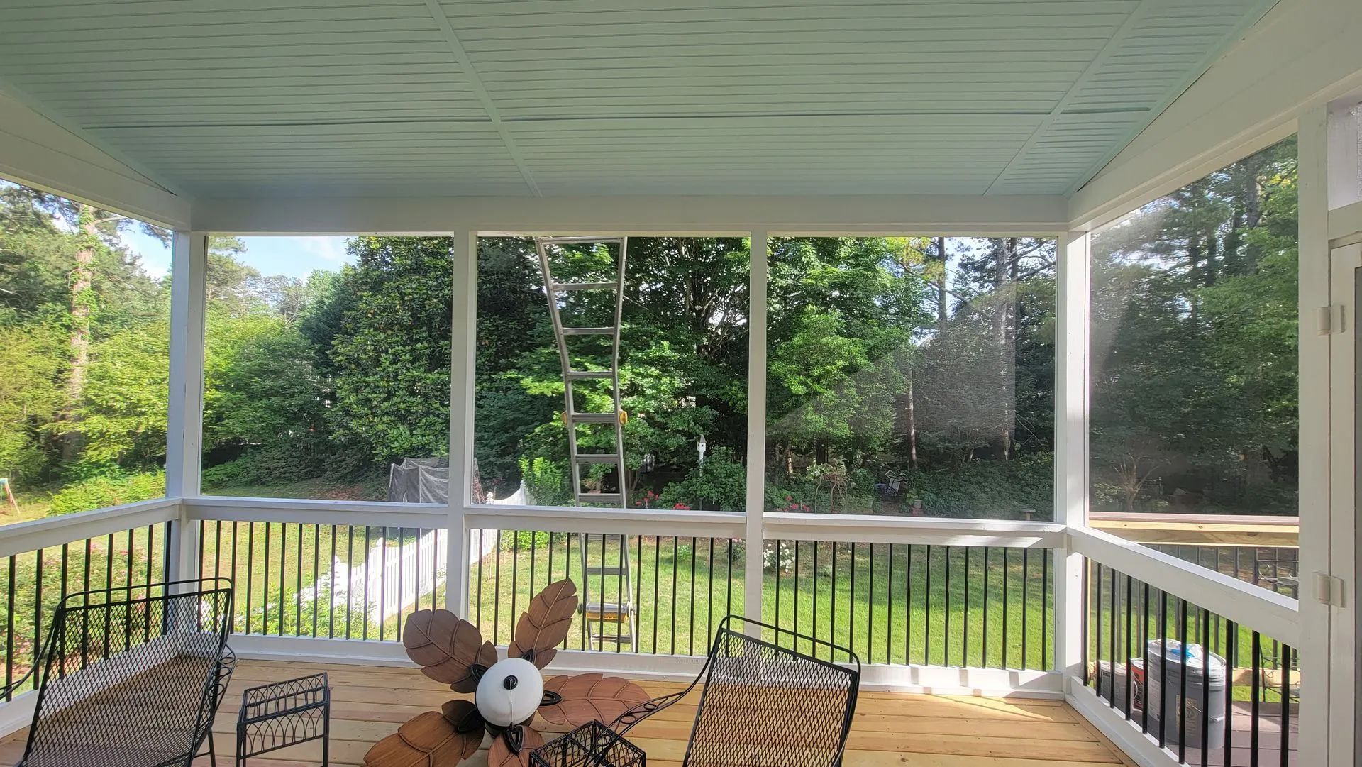 Screened porch with white trim, black railing, wooden floor, and view of green trees.