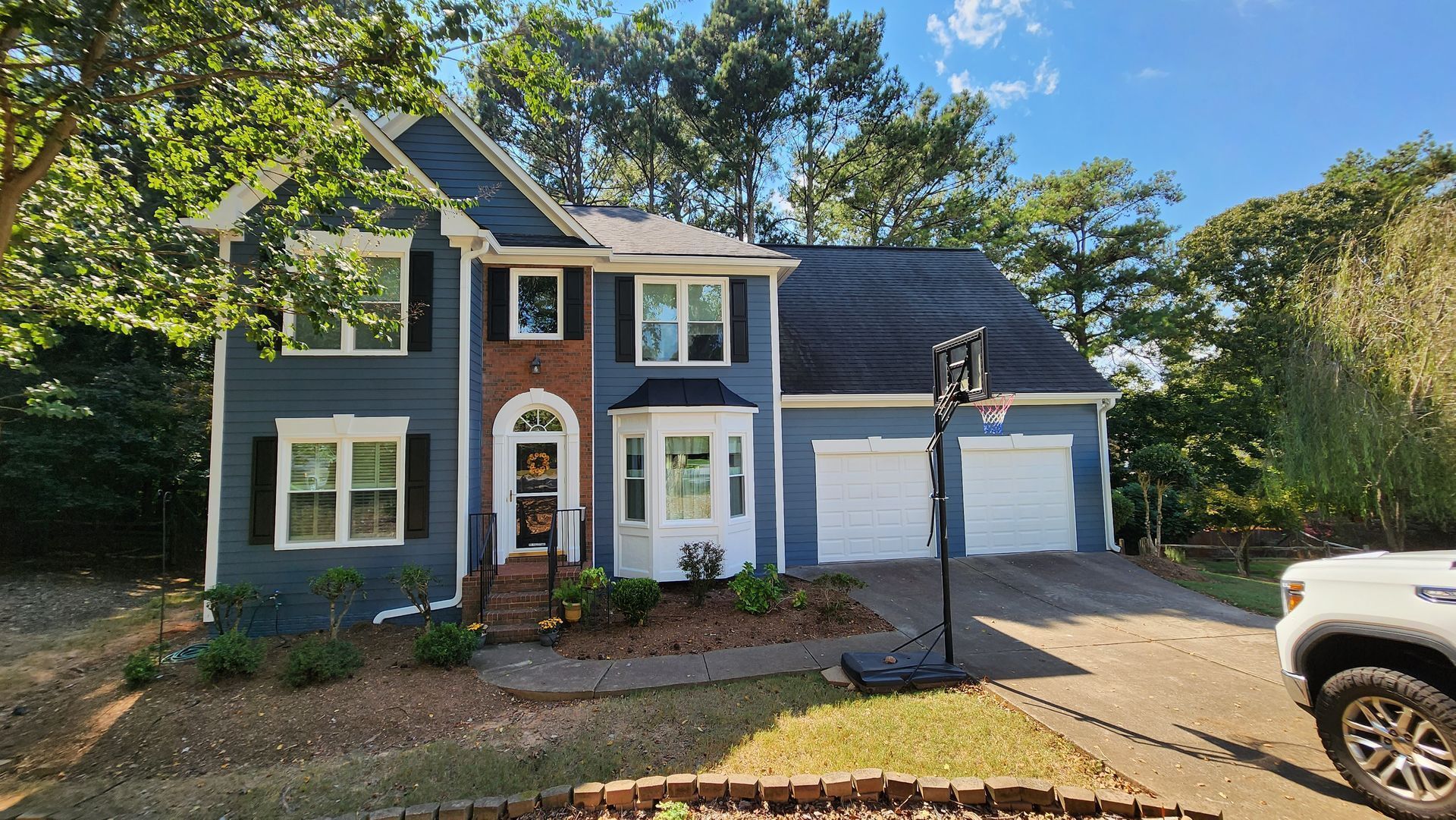 Two-story blue house with white trim, brick accents, and a basketball hoop in the driveway.