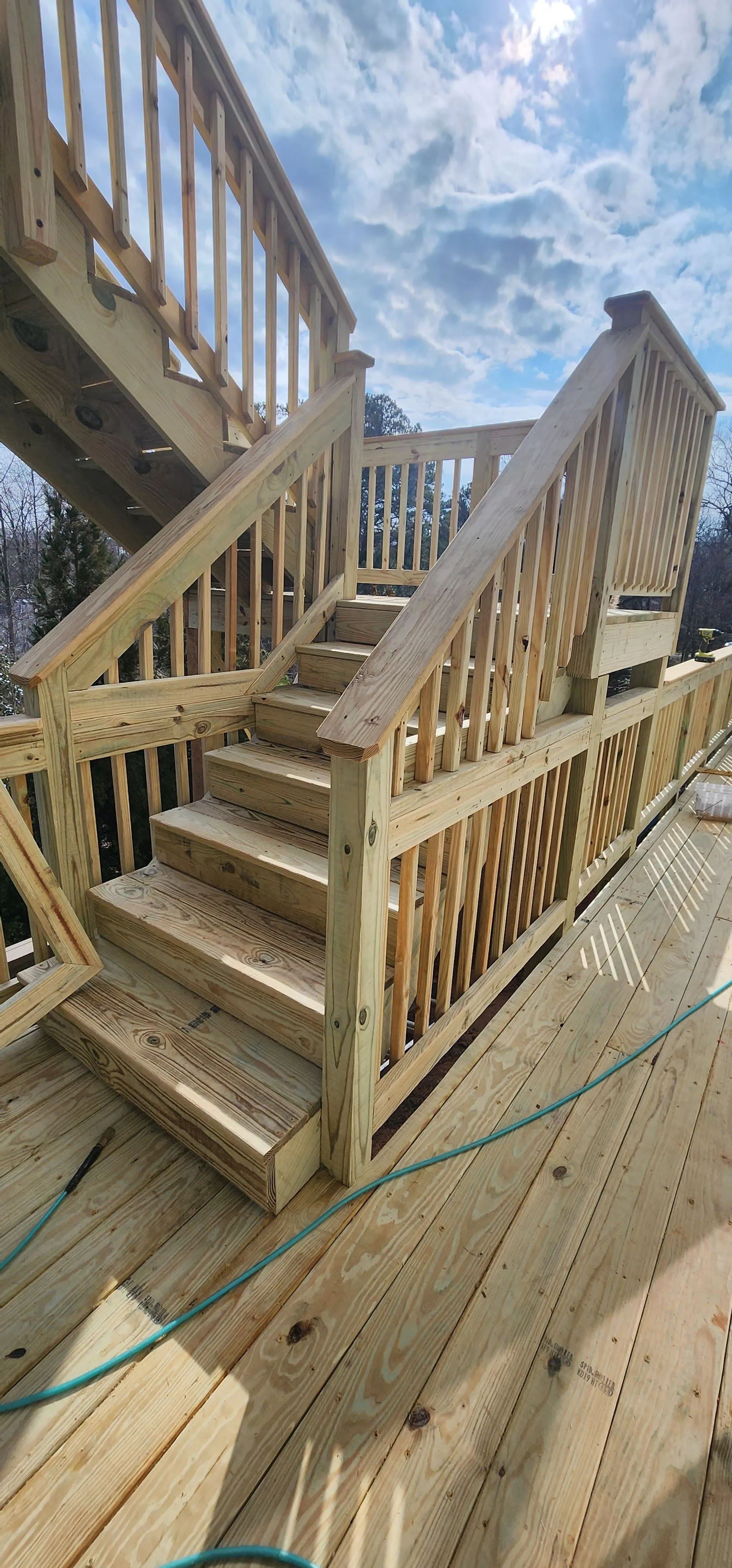 Wooden staircase leading up to a deck, with blue sky and clouds in the background.