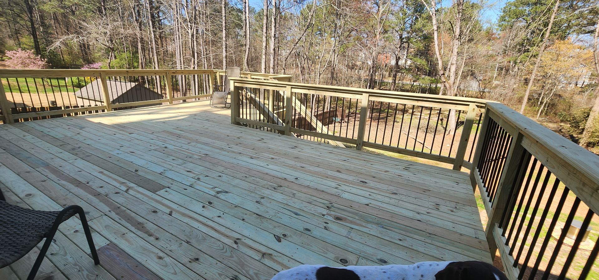Wooden deck with railings, trees, and a chair in a sunny outdoor setting.