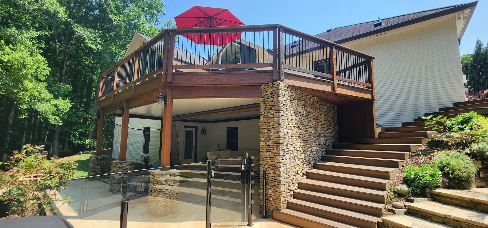A deck and stone structure house with steps and an umbrella on a sunny day.