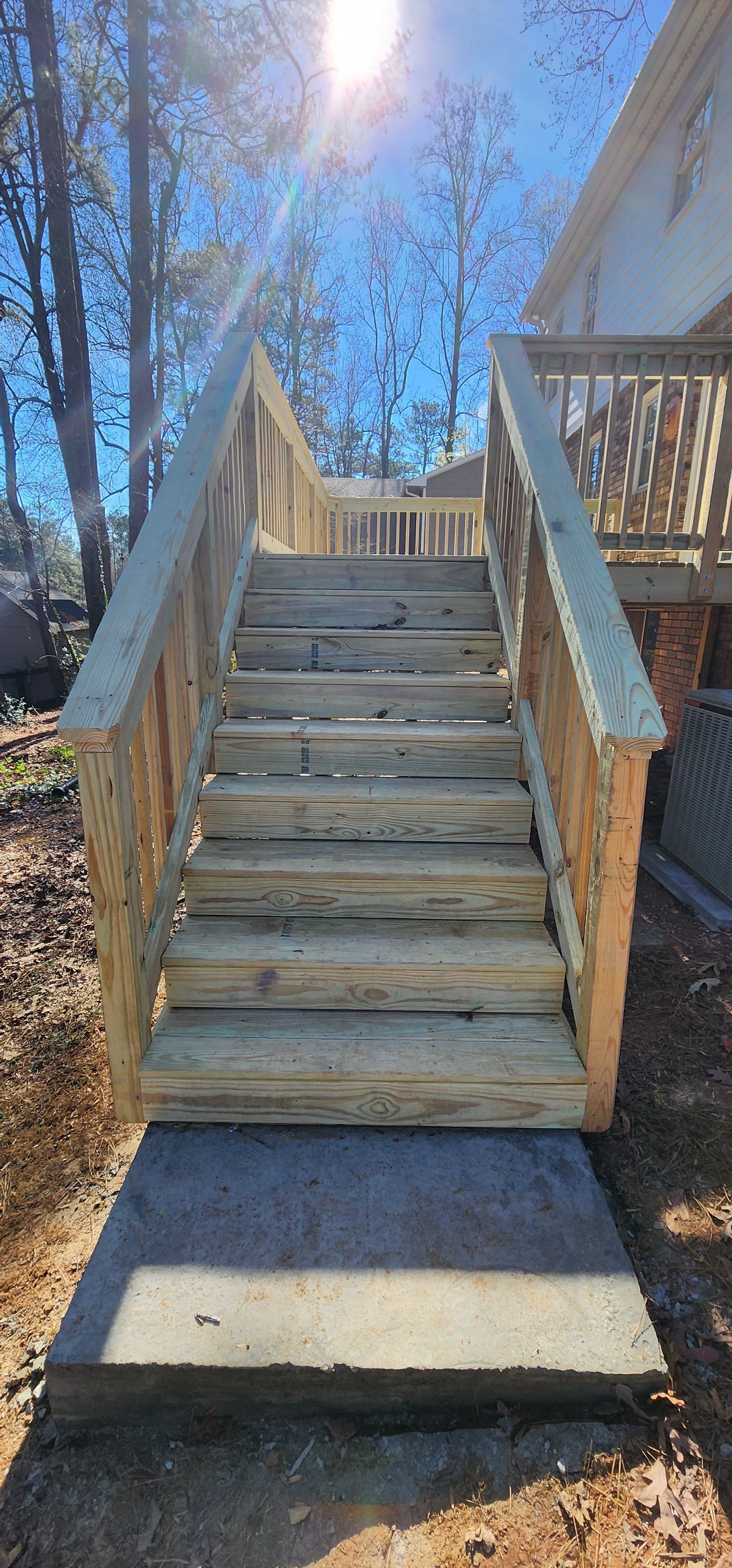 Wooden stairs leading up to a deck with sunlight in a blue sky.