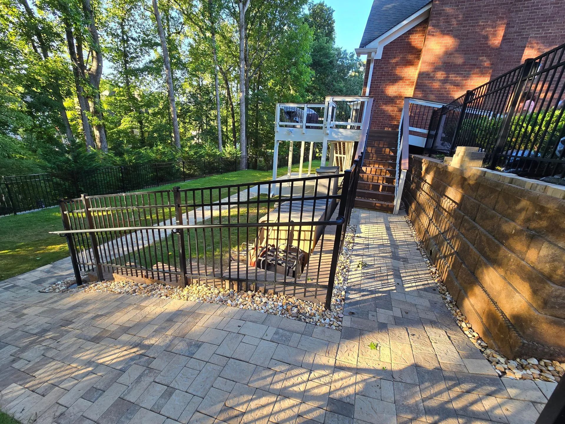 Brick patio with black fence and fire pit, leading to a wooden deck next to a brick house.