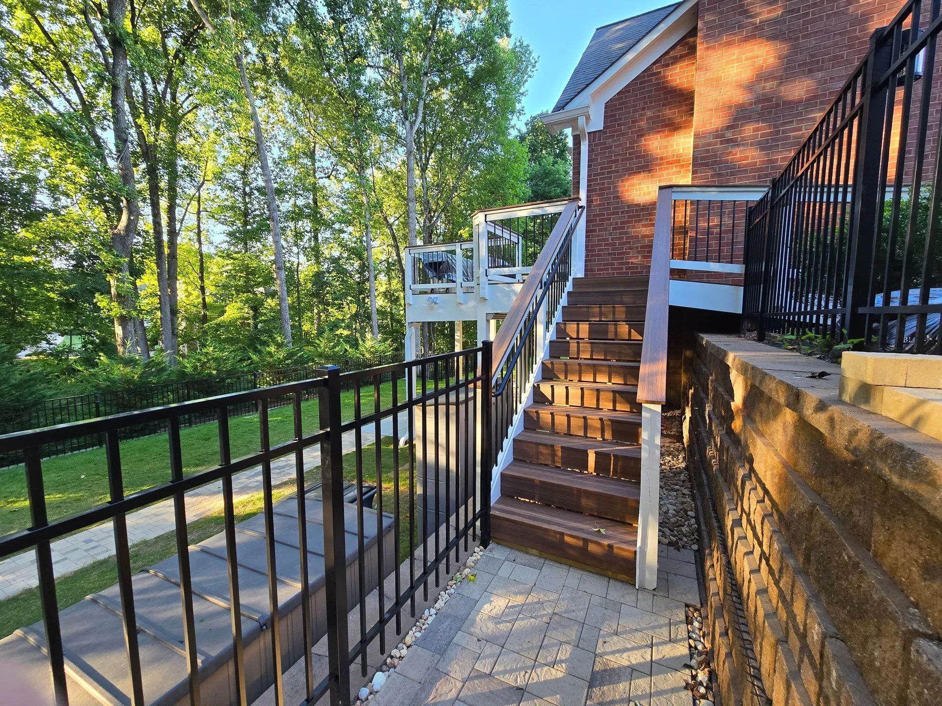 Brick house with wooden stairs, a deck, and black metal fencing on a sunny day.