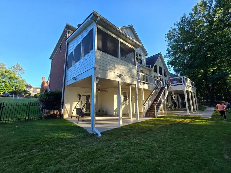 Backyard of a two-story house with a screened porch, deck, and grassy lawn under a blue sky.