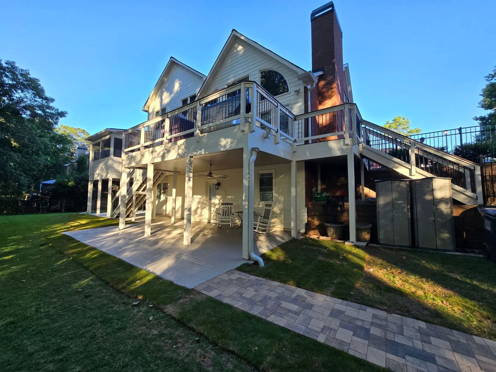 Two-story house with decks, patio, and brick path; sunny exterior.