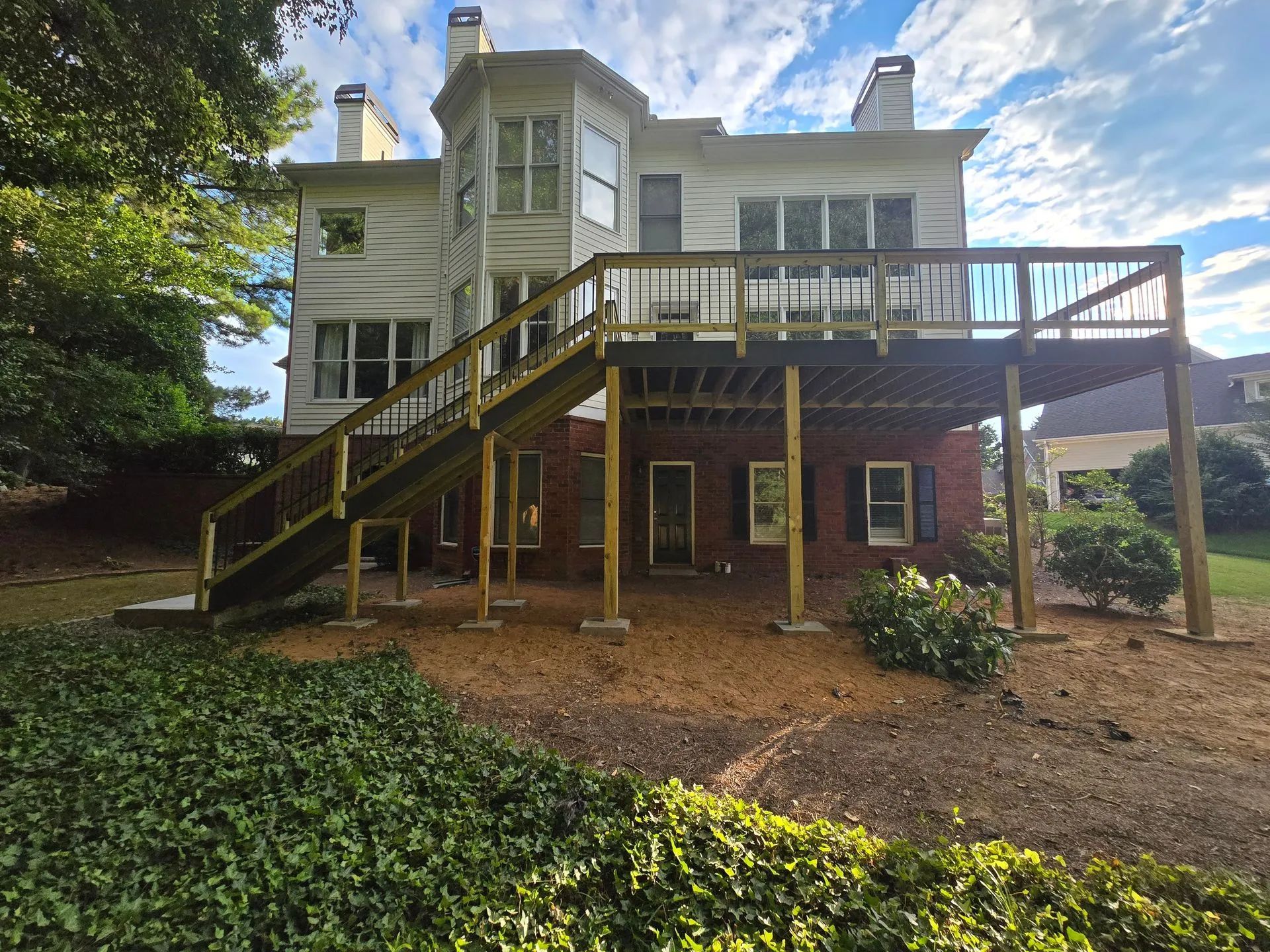 Back of a two-story house with a large wooden deck. The deck has stairs and supports over a brick foundation.