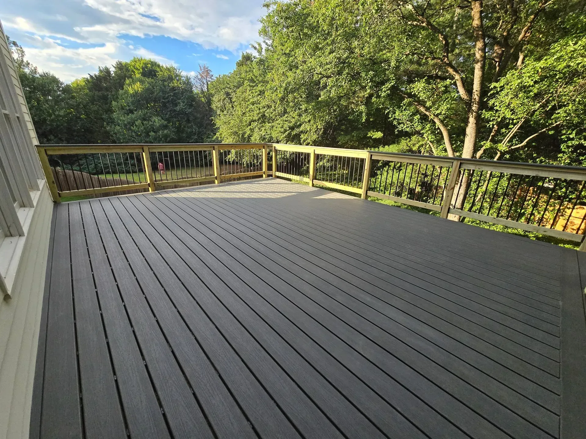 A large, gray composite deck with wooden railing, overlooking a wooded backyard.