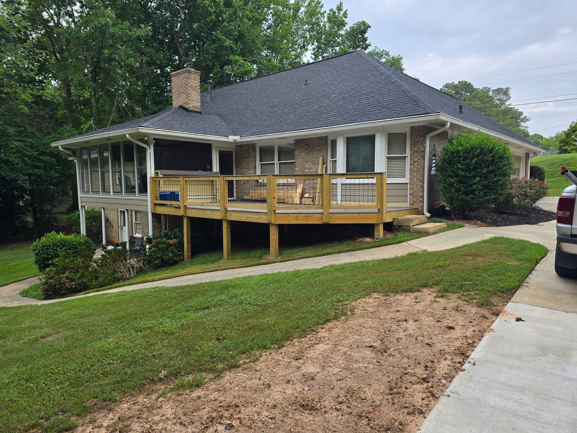 House with deck and screened porch, brick exterior, dark roof, surrounded by green grass and trees.