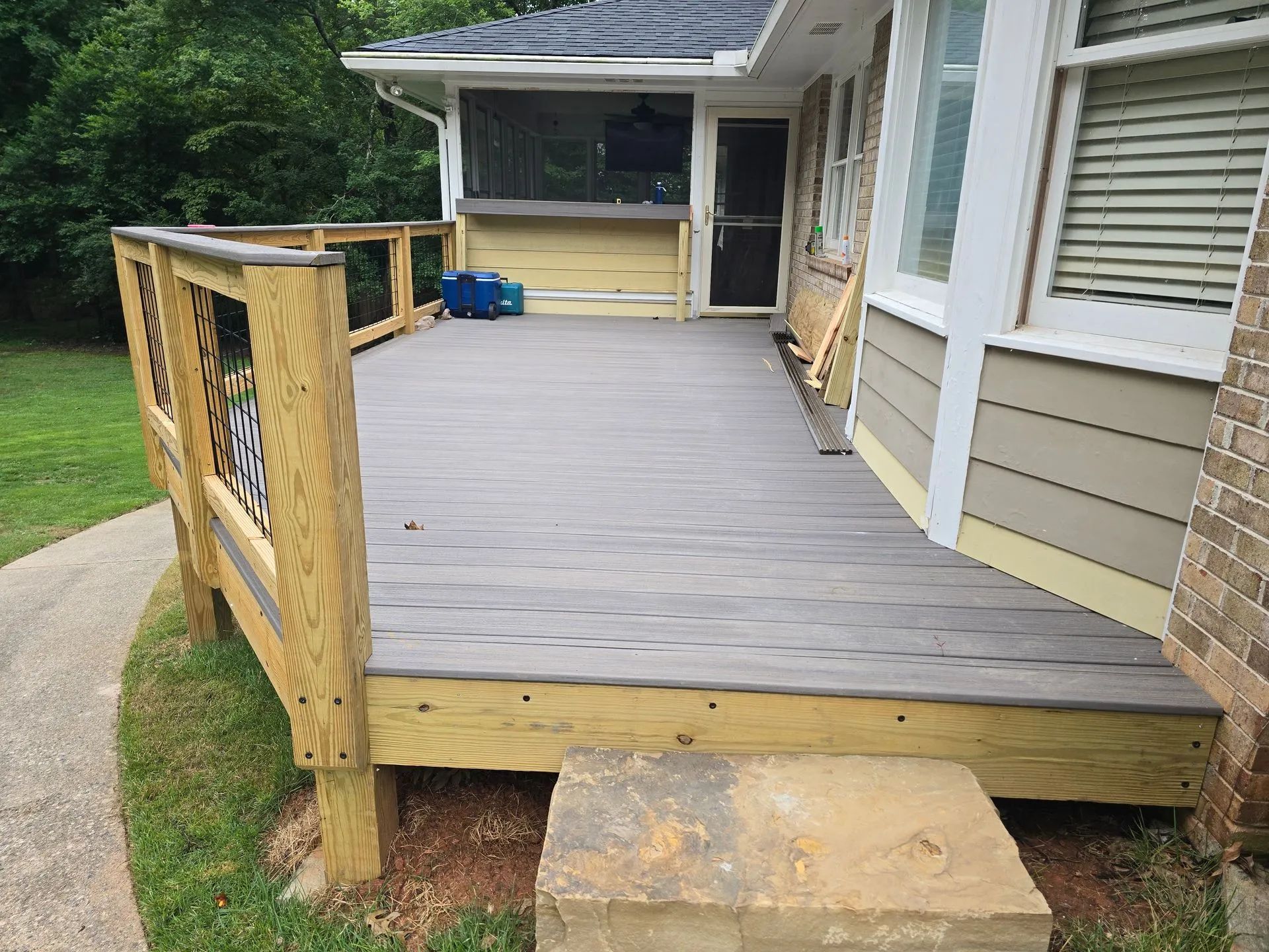 A deck with gray decking, a screened porch, and a concrete block base next to a house.