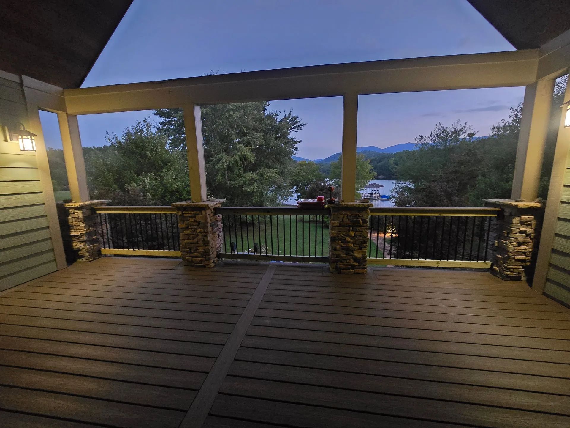 Wooden deck with a view of a lake and mountains at dusk. Lit by warm lights.