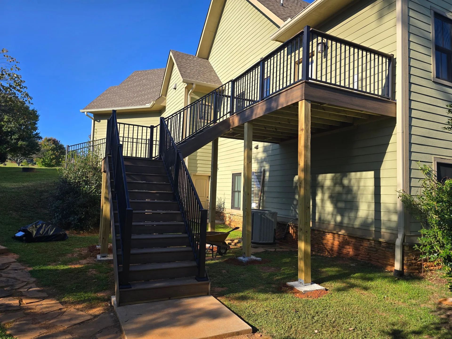 A wooden deck and stairs attached to a two-story house; black railings, green siding.