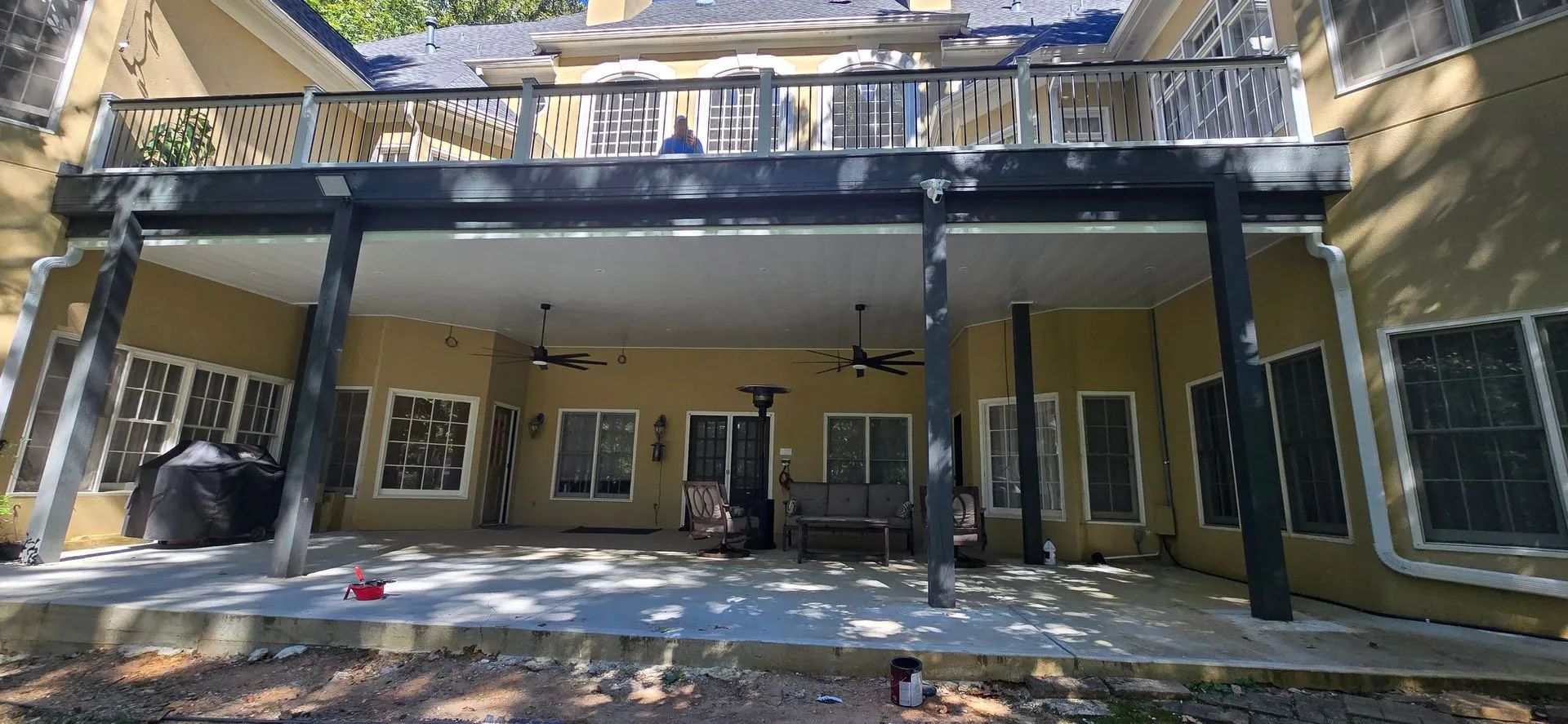 Backyard patio with a second-story deck; beige exterior walls, black columns, and a concrete patio.