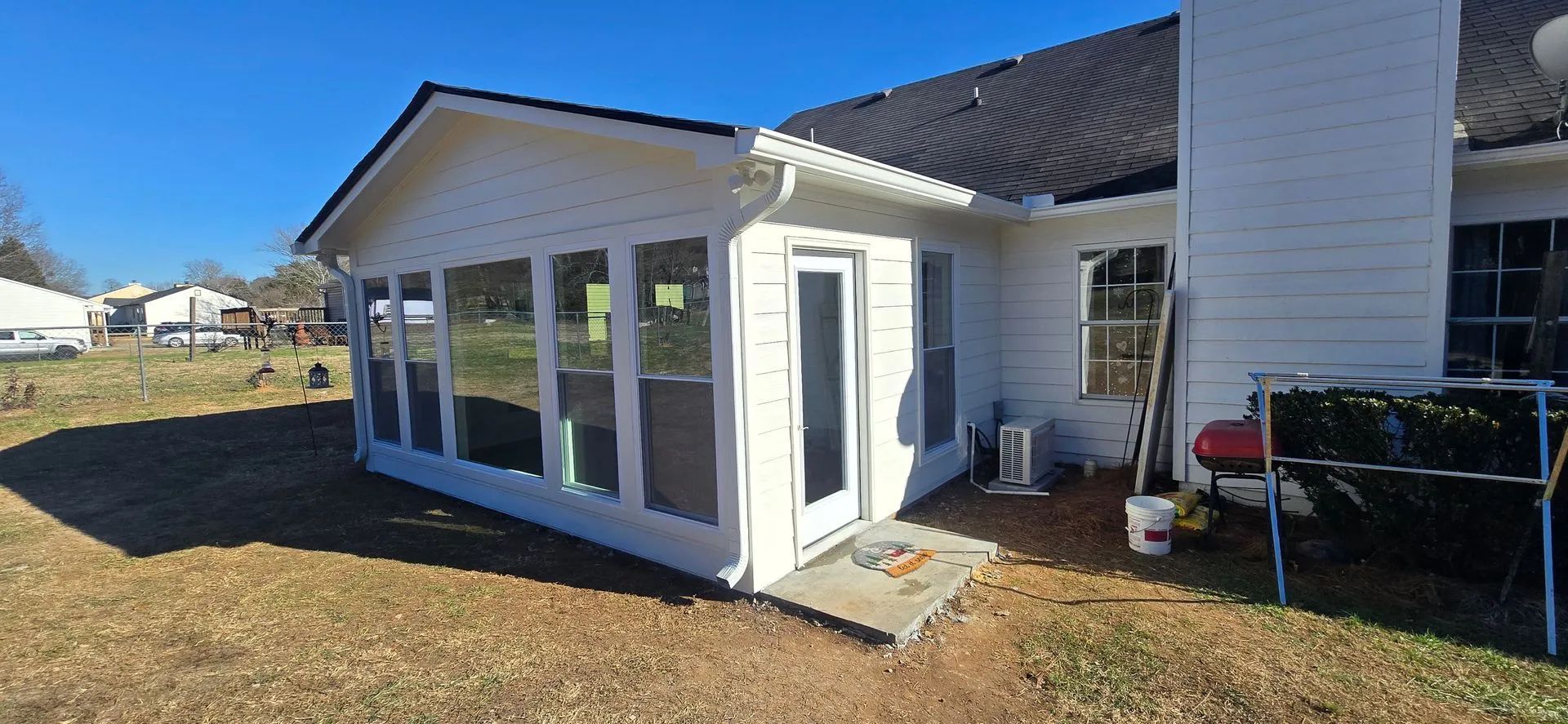 A white house with a sunroom, door, and chimney on a sunny day.