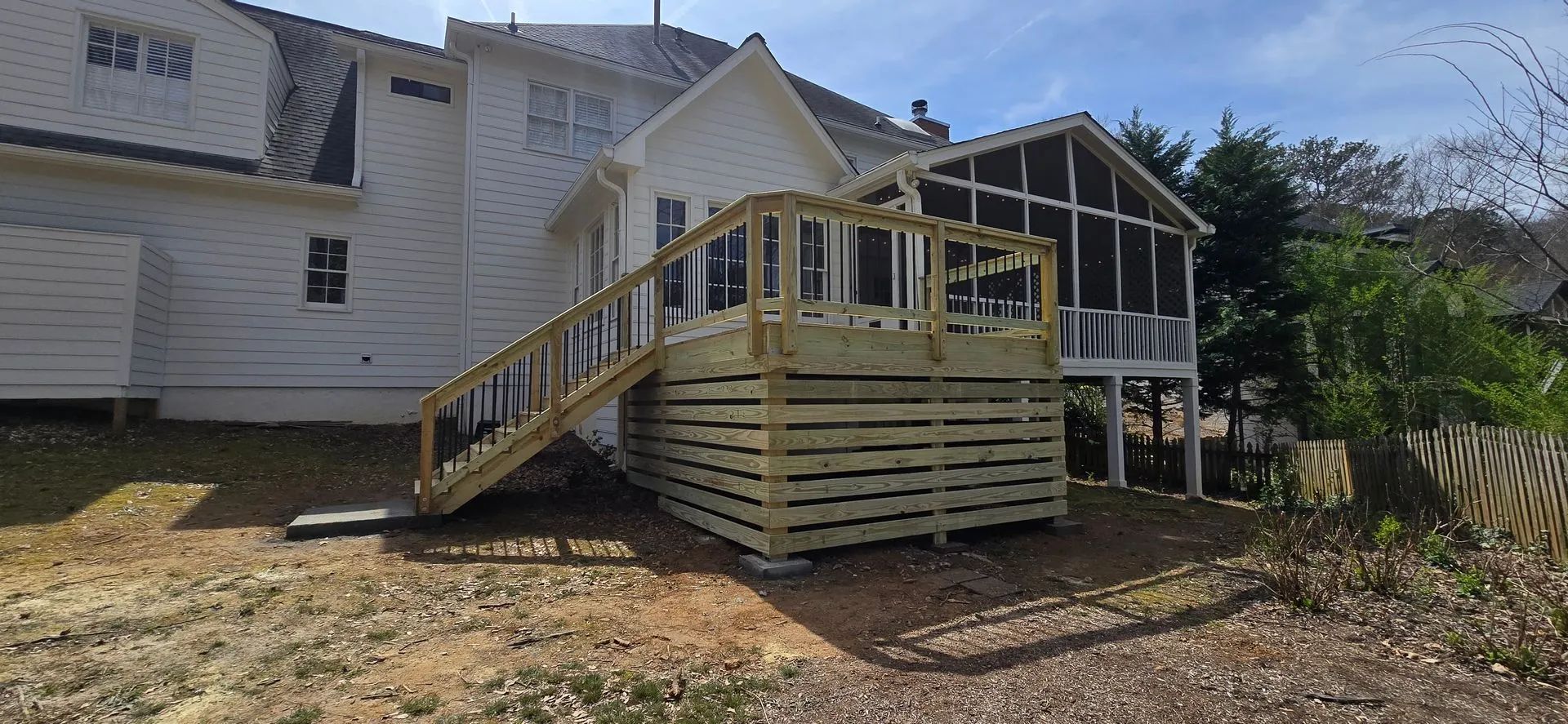 A new wooden deck and stairs next to a white house and a screened porch.